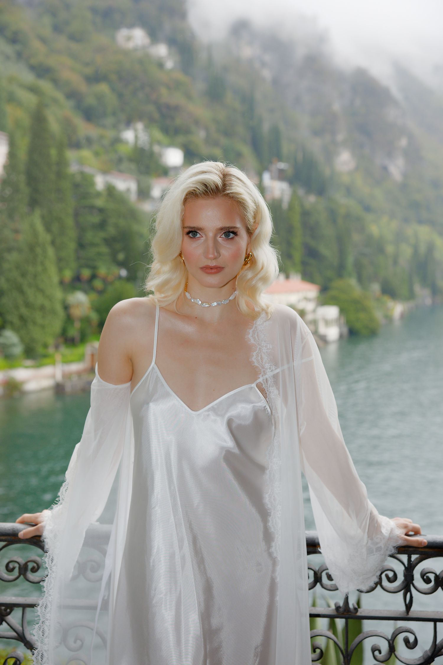 Elegant white silk dress against scenic mountain lake backdrop in luxurious European setting.
