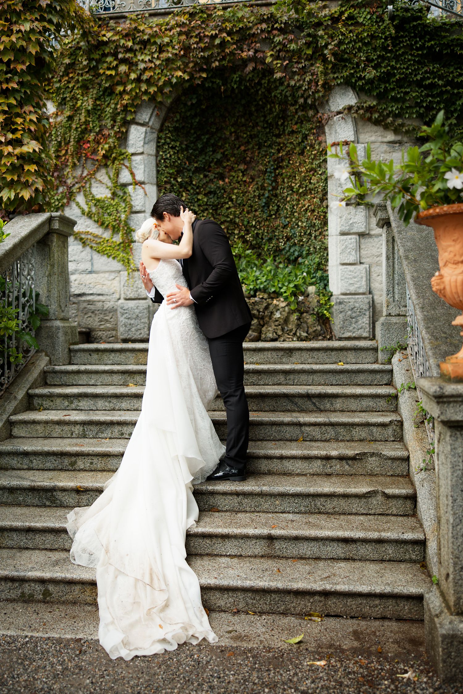 A wedding couple shares an intimate moment on ivy-covered stone stairs.