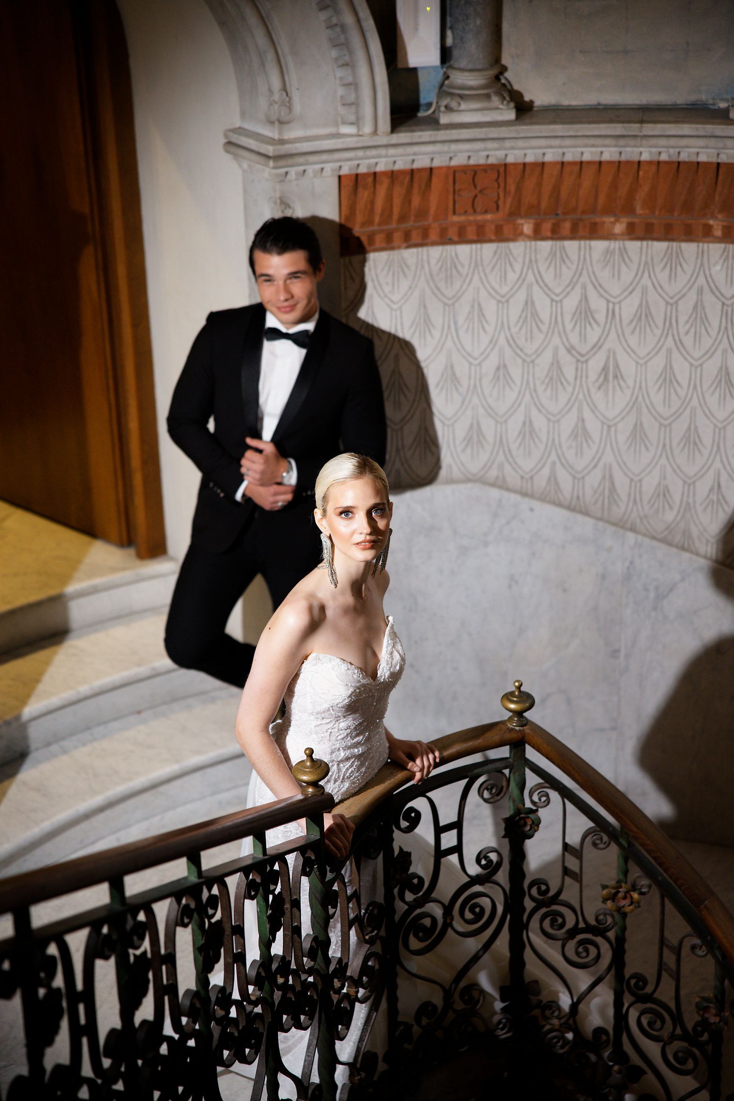 Wedding couple posing on an elegant staircase with ornate iron railings.