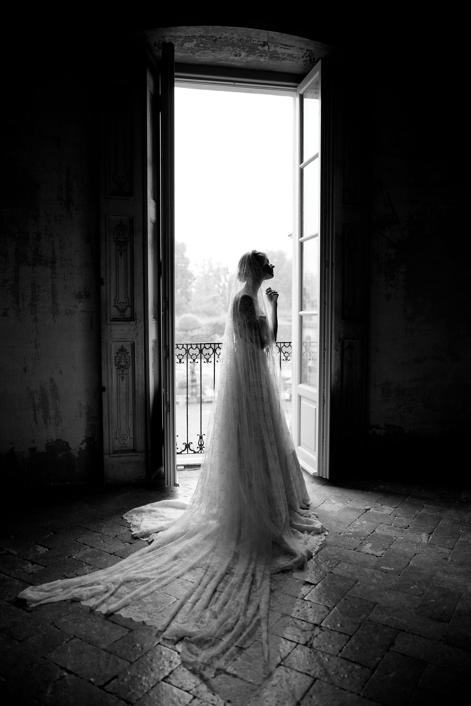 Silhouette of person in flowing white wedding dress standing in dramatic doorway overlooking balcony.