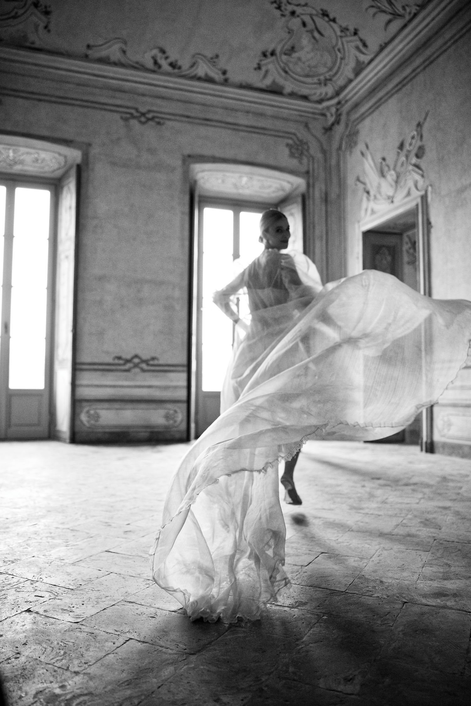 Black and white photo of flowing dress spinning in motion inside ornate vintage ballroom.