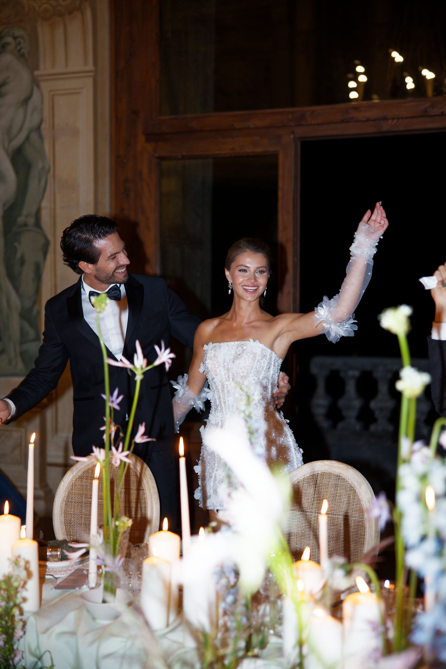 Wedding celebration at an ornate venue with candlelit table and floral arrangements.