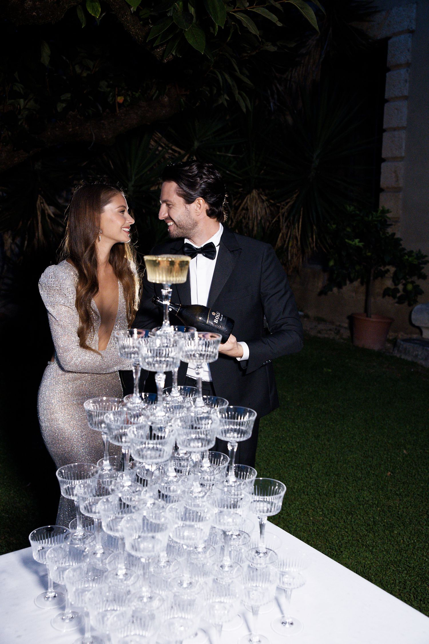 Couple stands beside champagne tower display at formal event.