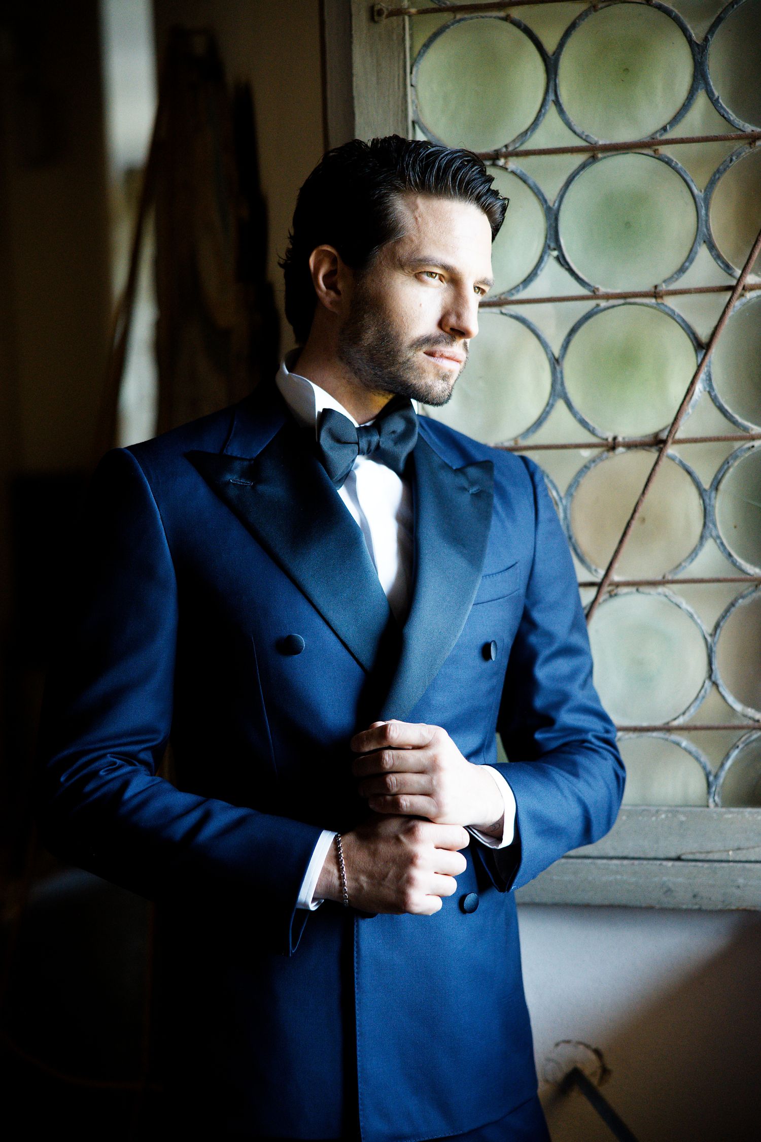 Formal portrait by a window showing a navy blue double-breasted tuxedo with black bow tie.