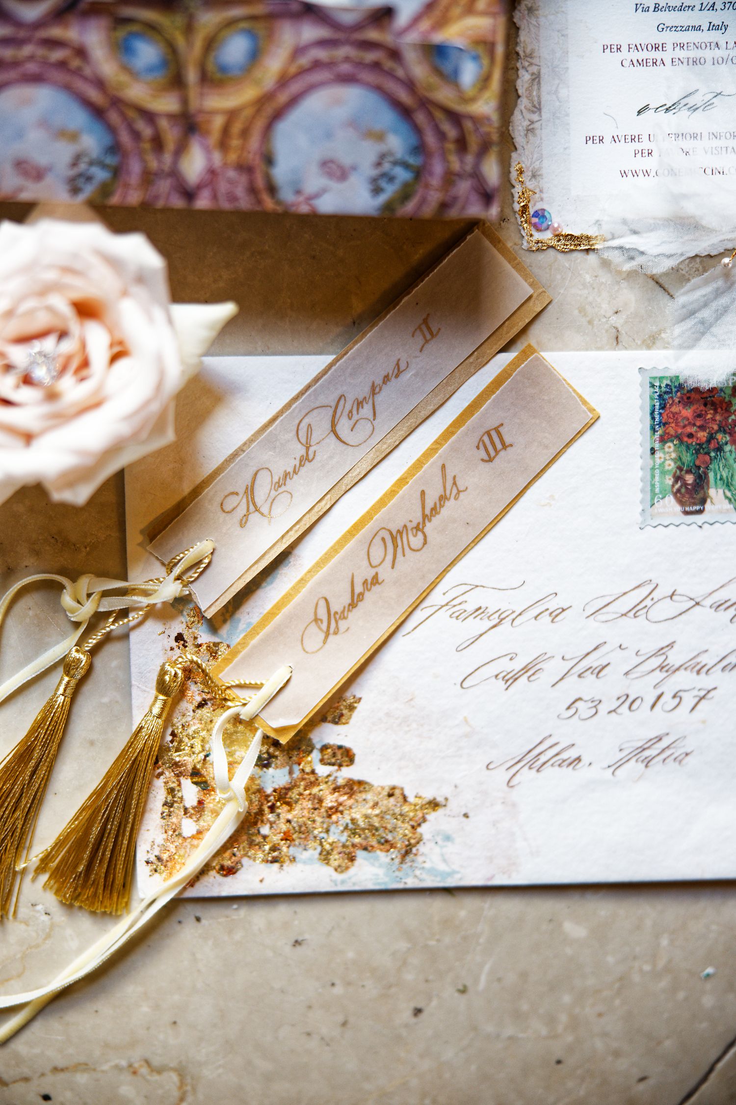 Elegant wedding stationery with gold tassels and calligraphy detail on cream paper.