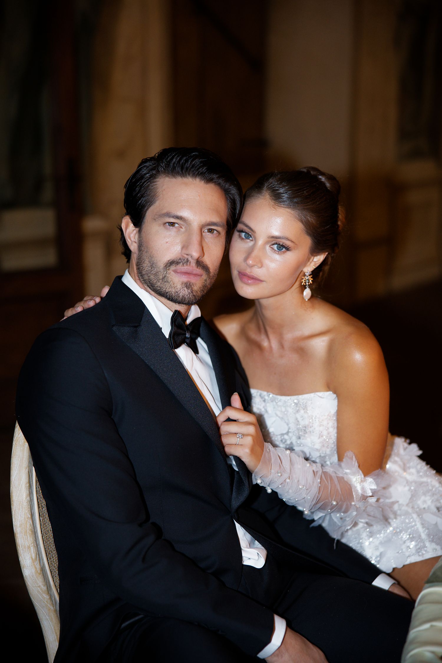 Elegant couple in formal evening wear pose together, with bride in white dress and groom in classic black tuxedo.