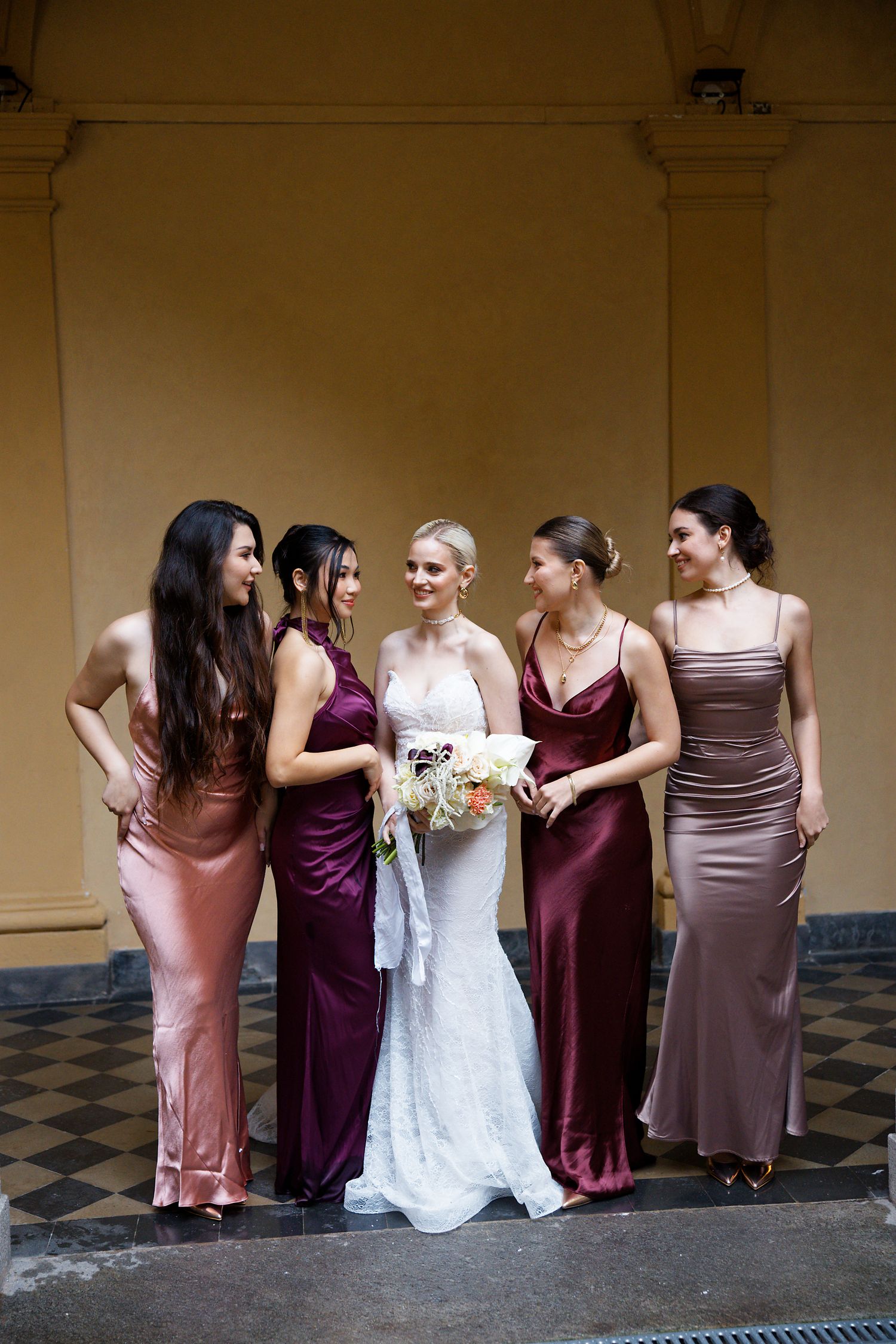 Wedding party in elegant jewel-toned dresses standing together under an archway.