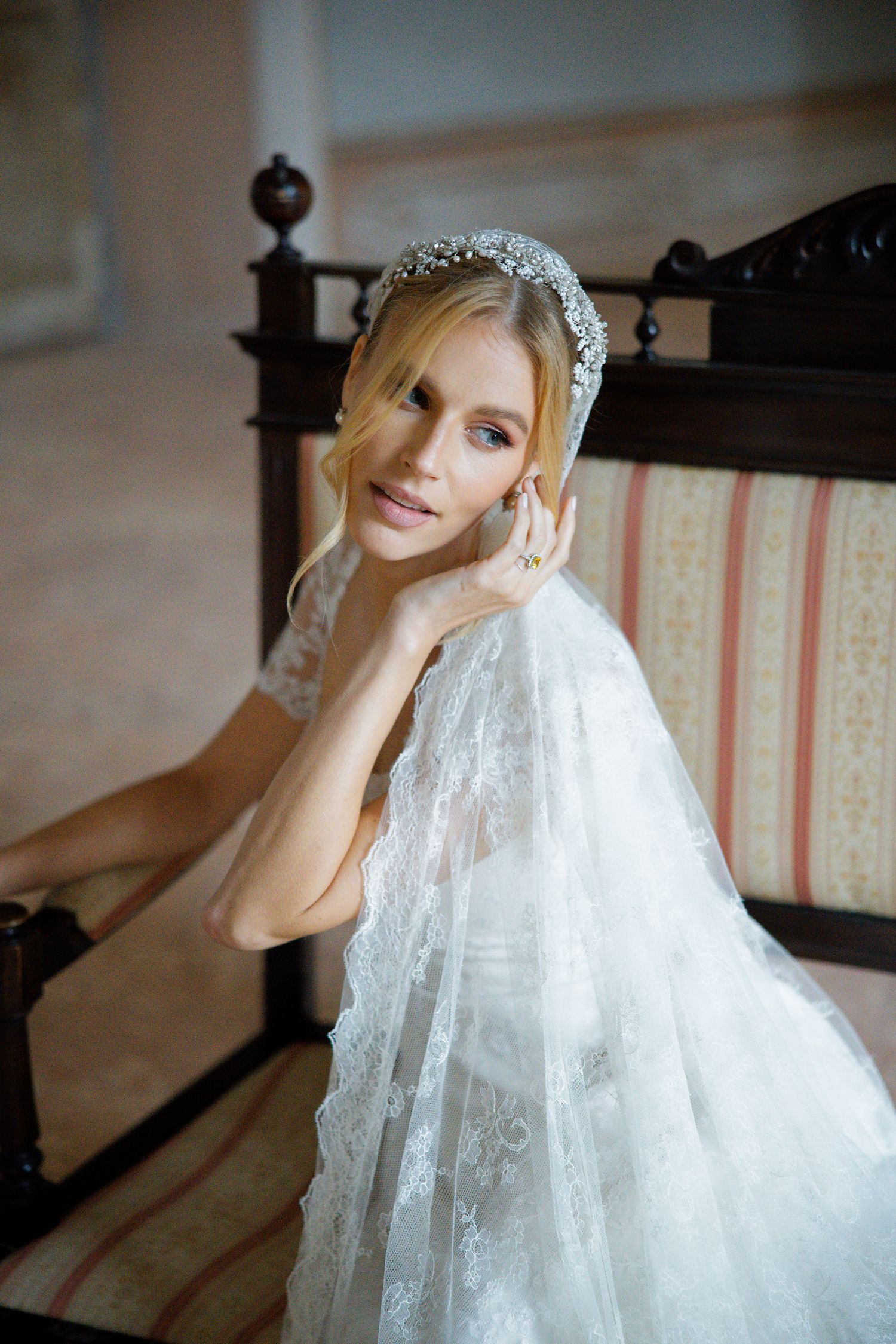 Ethereal bridal portrait with flowing veil and crystal headpiece against vintage furniture.
