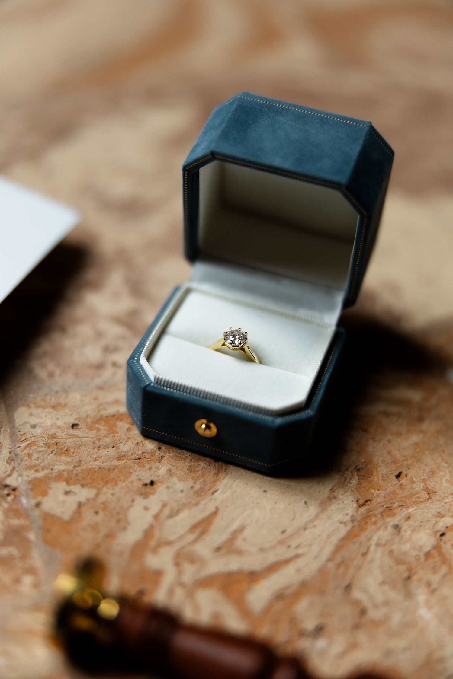Diamond engagement ring in a navy blue velvet box photographed on a brown surface.