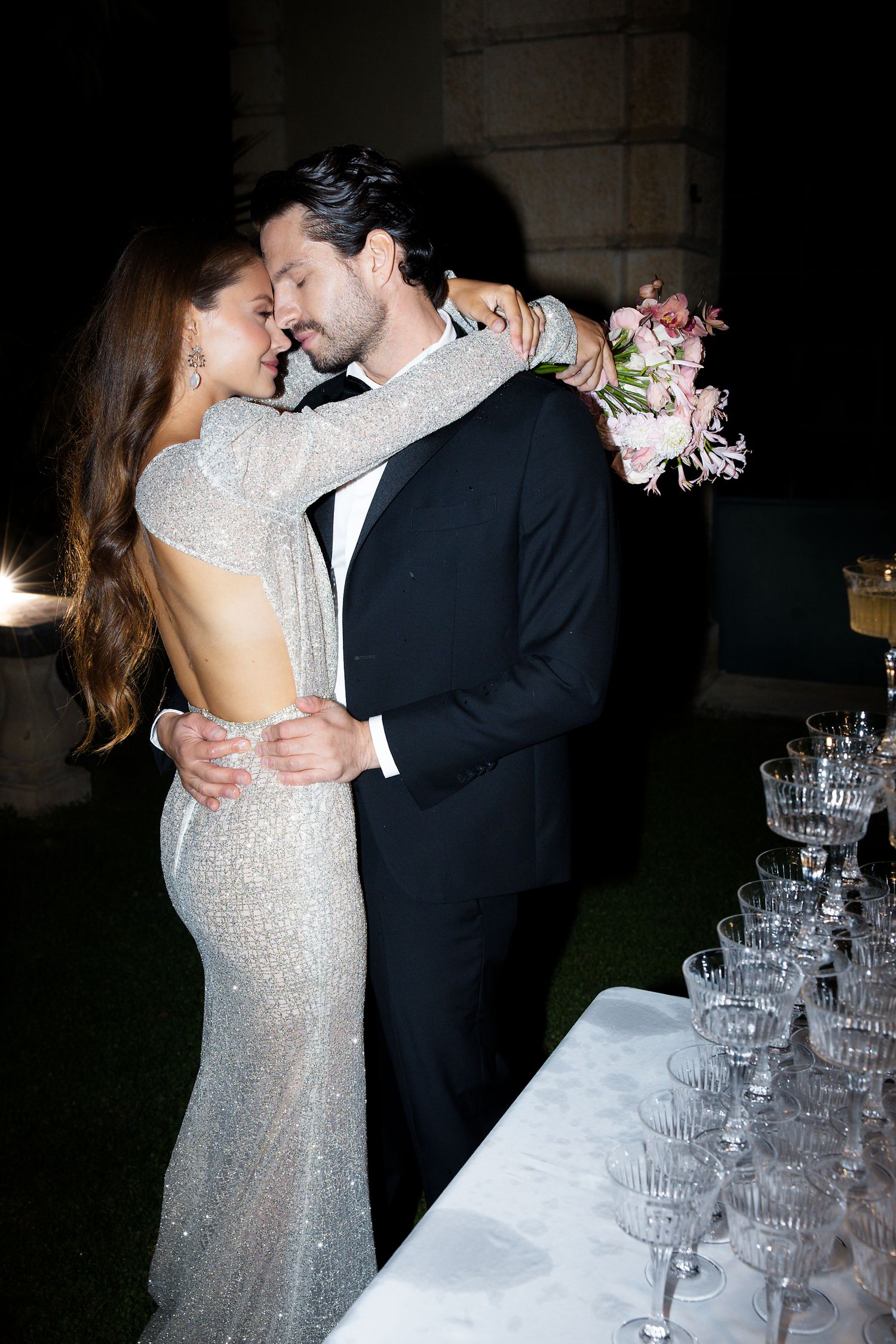 Couple in formal attire sharing an intimate moment beside a champagne tower at their wedding celebration.