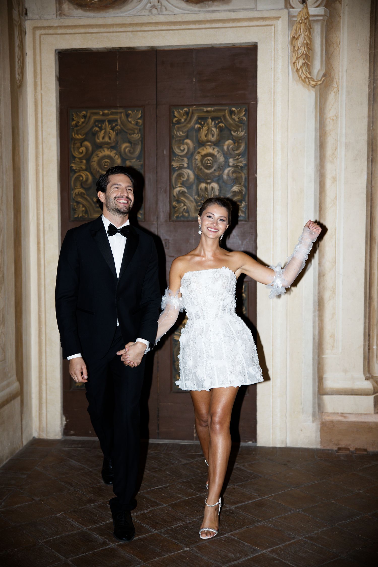 Joyful newlyweds walking through elegant hallway in wedding attire.