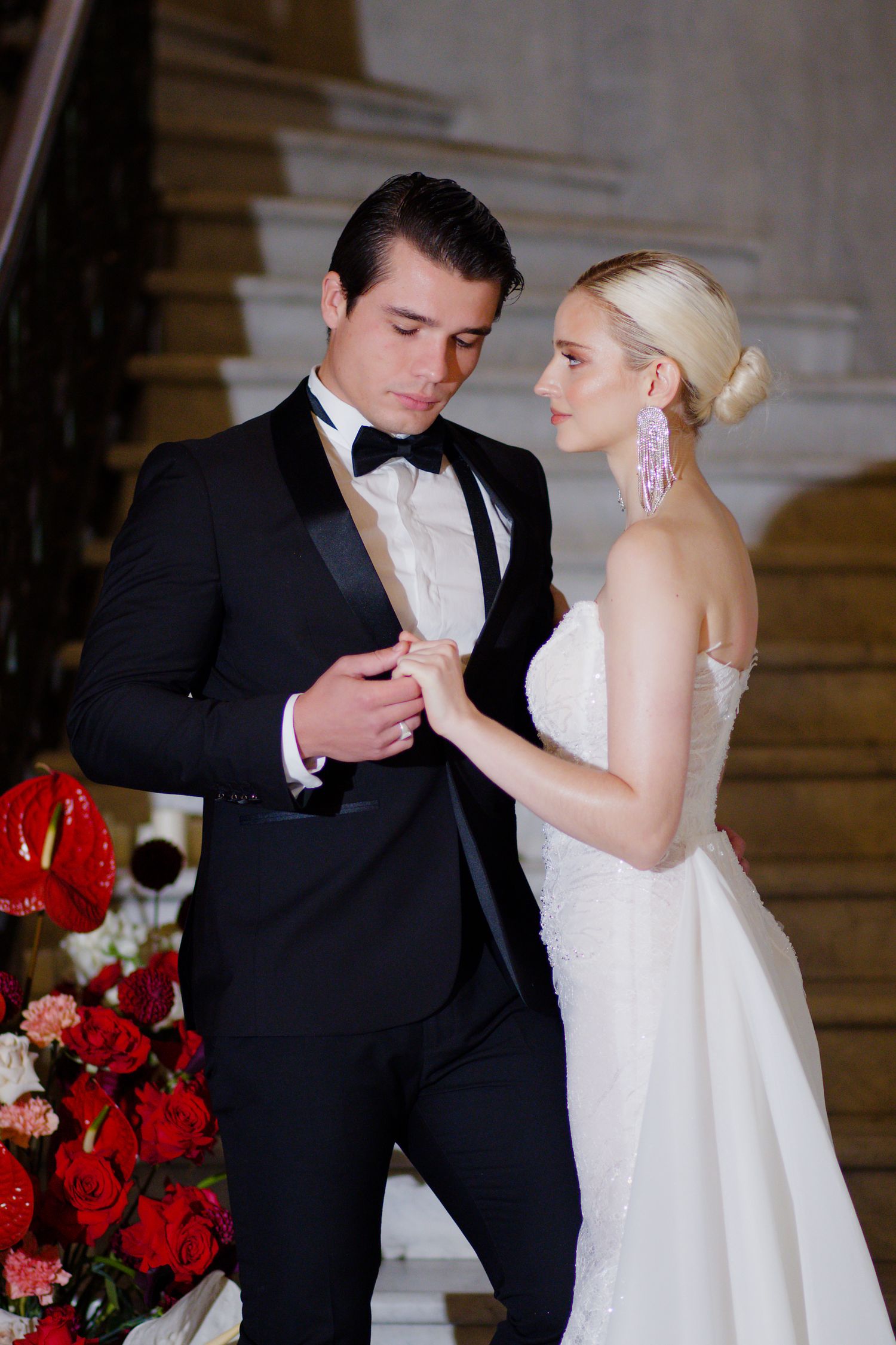 Intimate moment captured on grand staircase with red rose floral decorations.