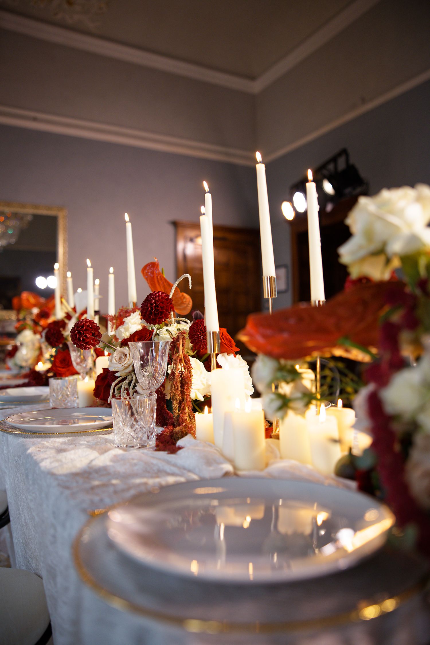 Elegant wedding table setting with white candles, lace tablecloth, and floral arrangements in romantic lighting.