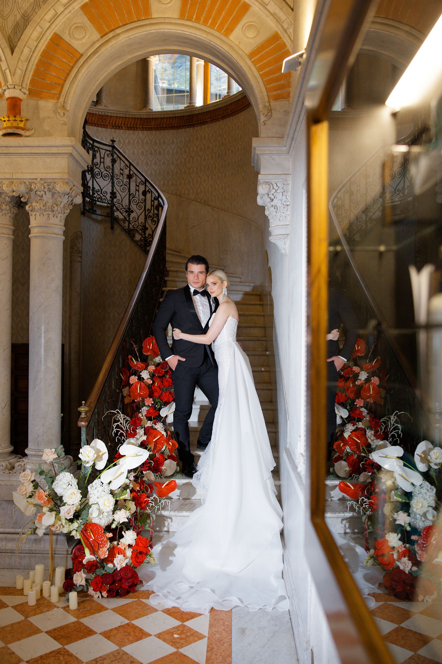 Wedding couple on marble staircase with red and white floral arrangements.