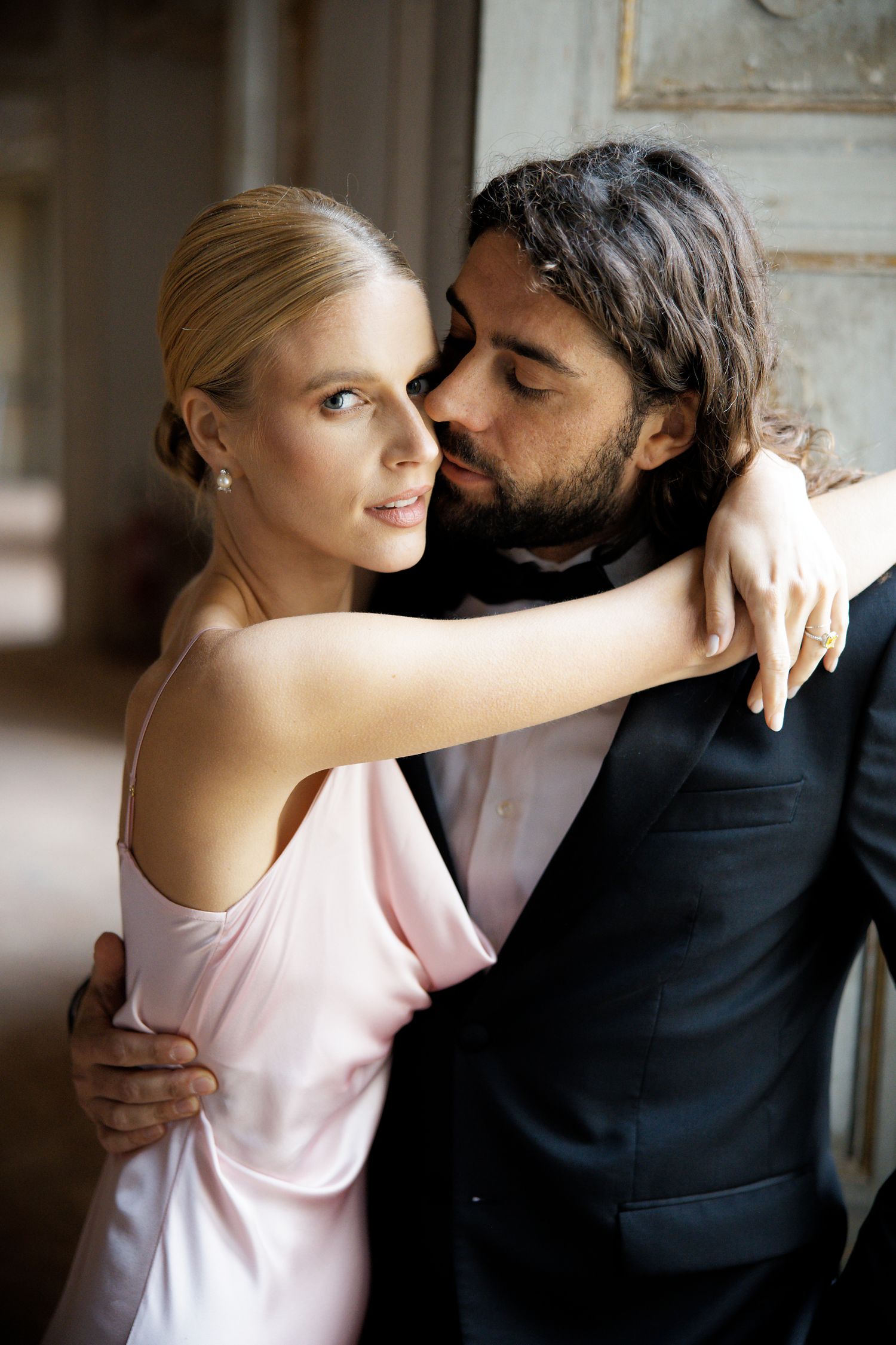 A tender embrace between a couple in formal attire against a classic interior backdrop.