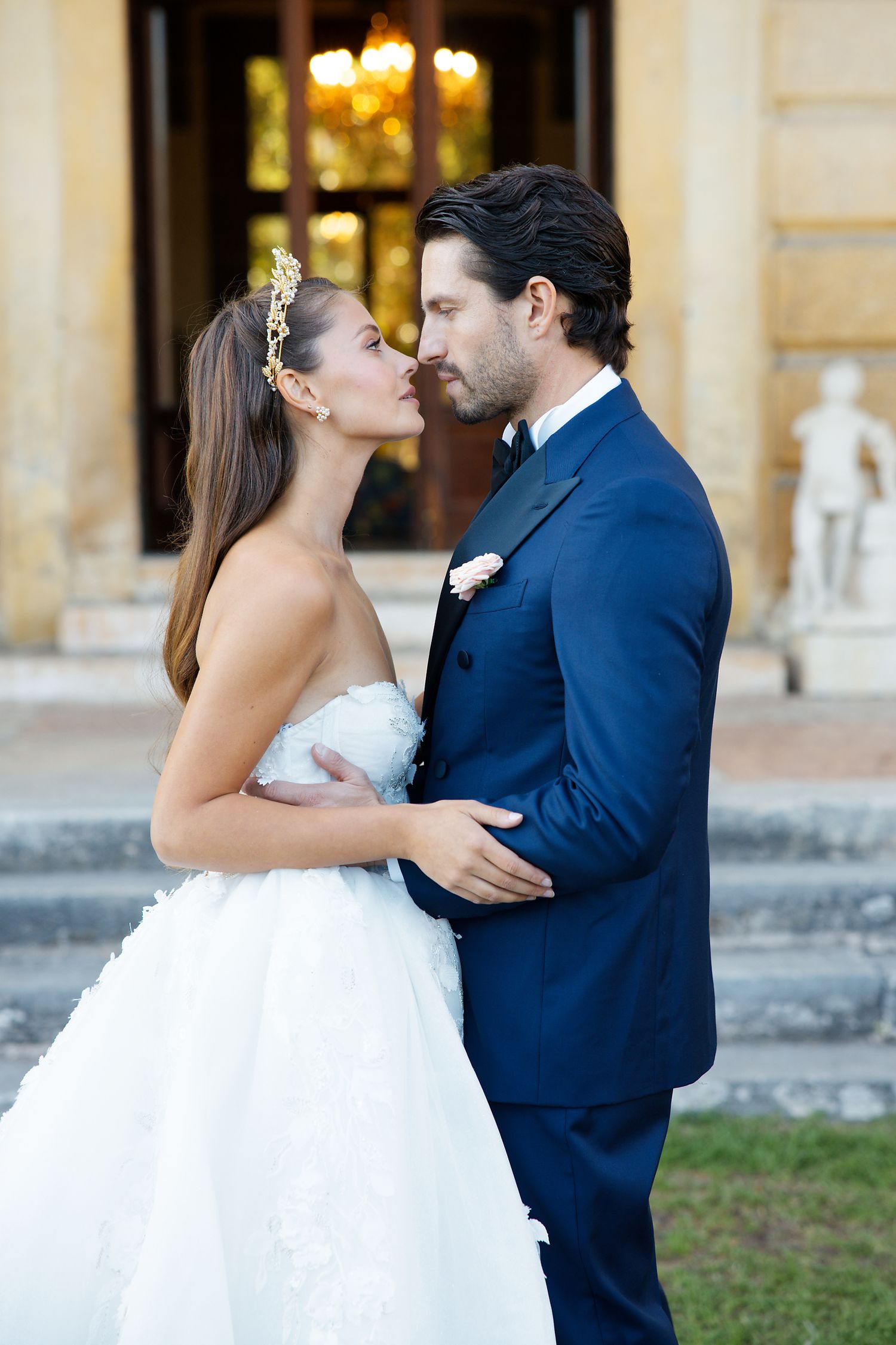 A romantic wedding photo of a couple sharing a tender kiss, with the bride in white and groom in navy blue.