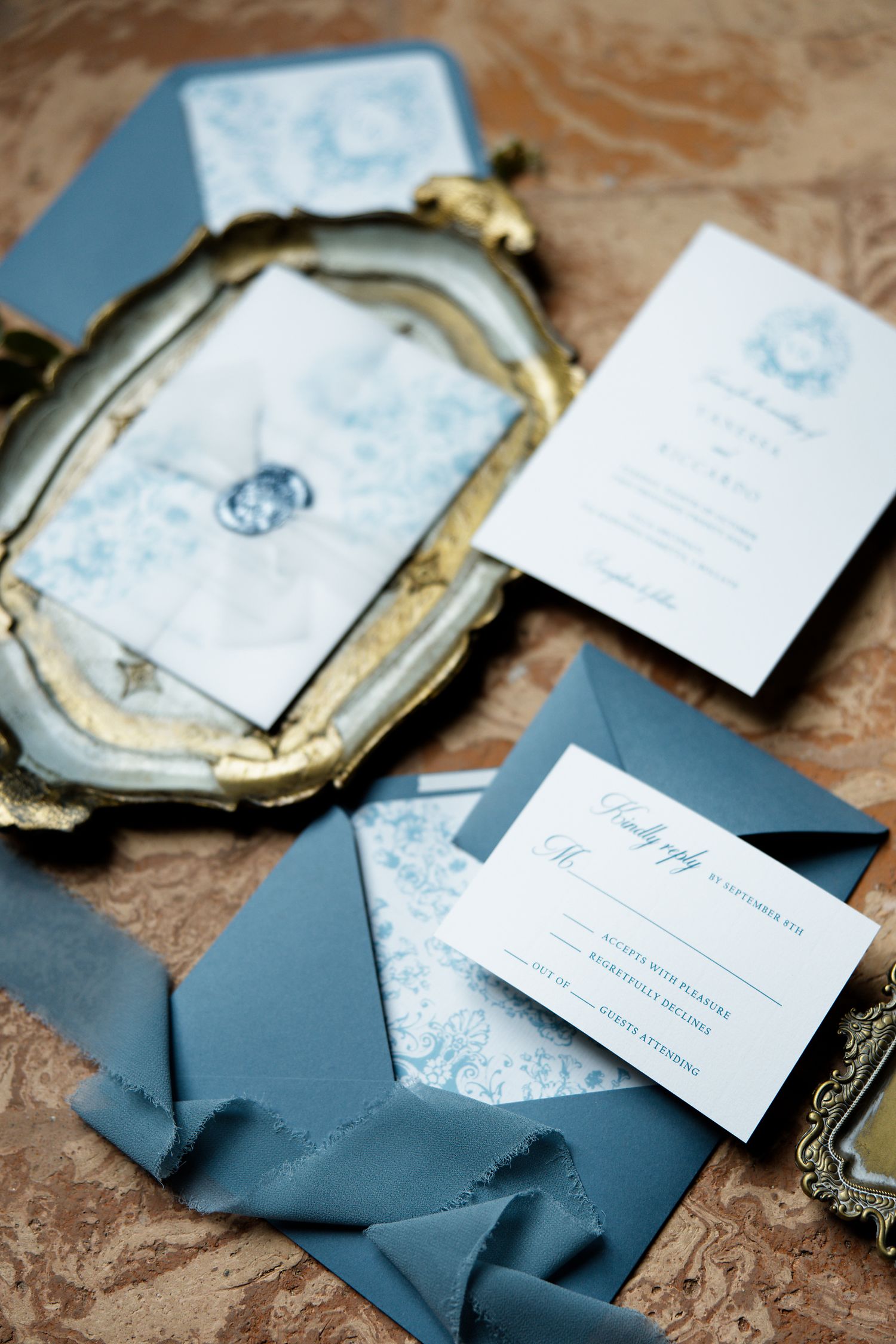 Close-up of vintage-style wedding stationery with blue and white design on antique gold tray.