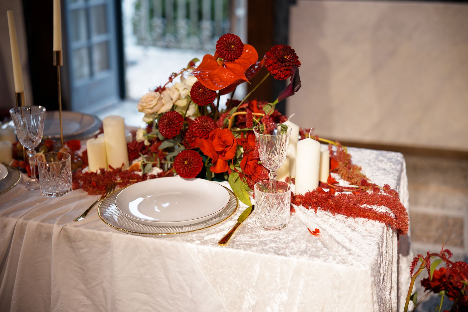 Elegant wedding table decorated with red floral arrangements, candles, and gold-rimmed place settings.