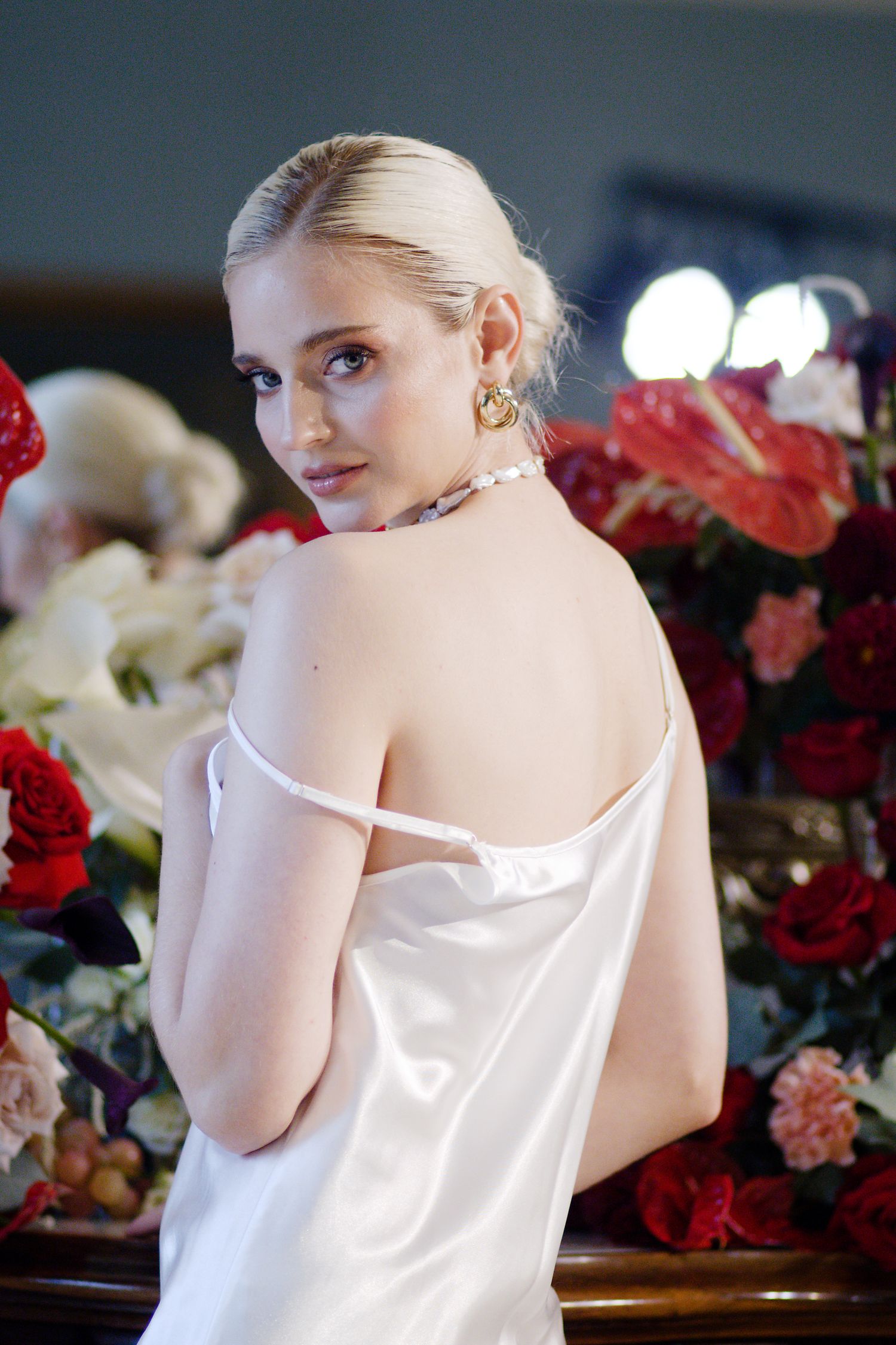Elegant white silk dress photographed against dramatic red and white floral arrangement.