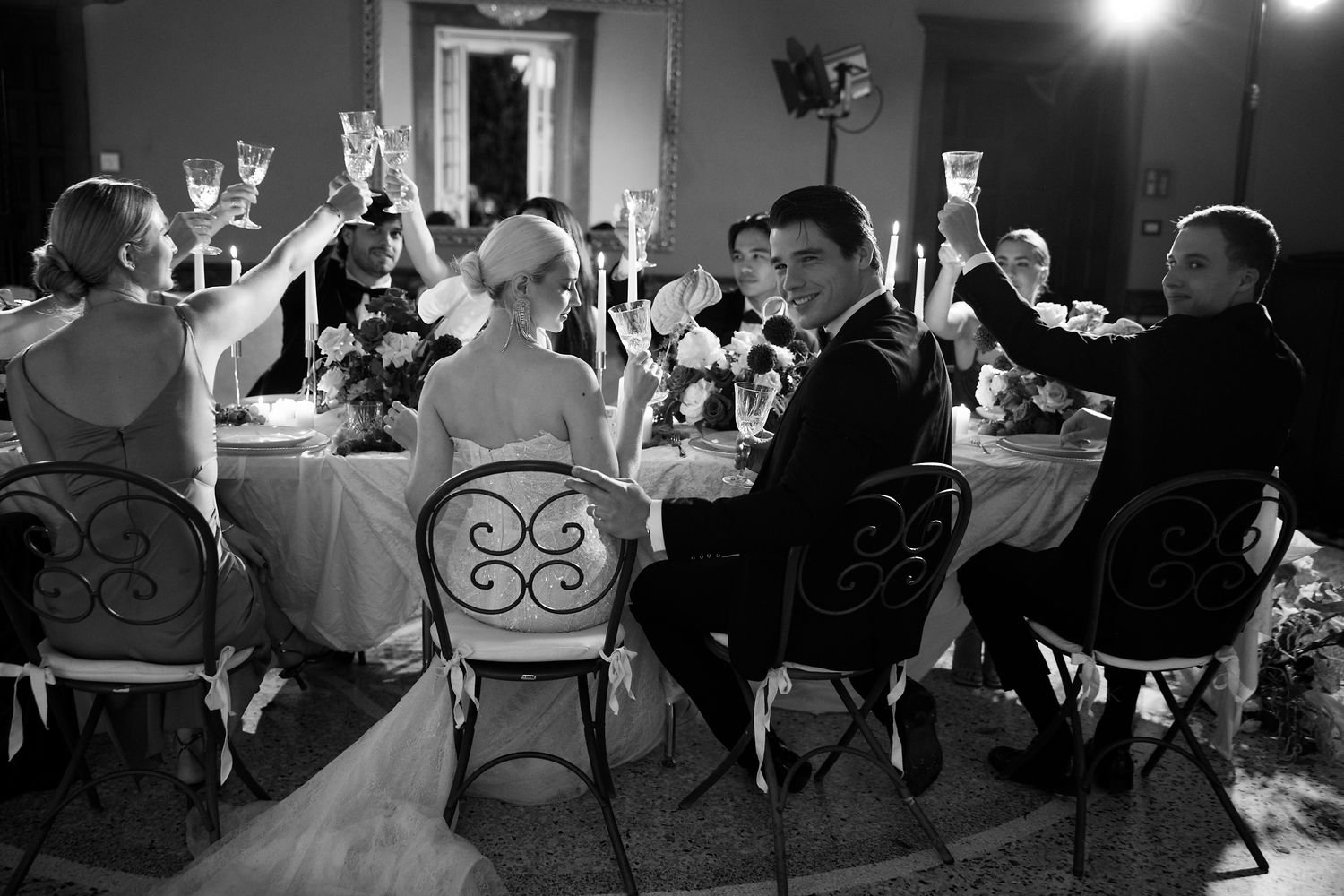 Black and white reception photo showing wedding guests raising glasses in celebration.