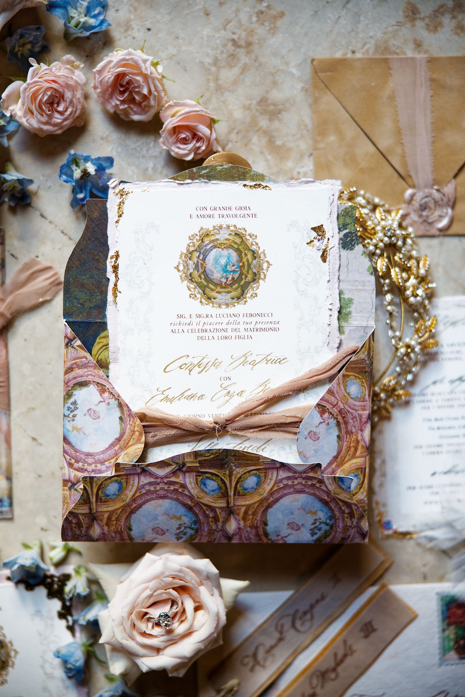 Ornate wedding invitation with pink roses and blue details features gold foil nest design.