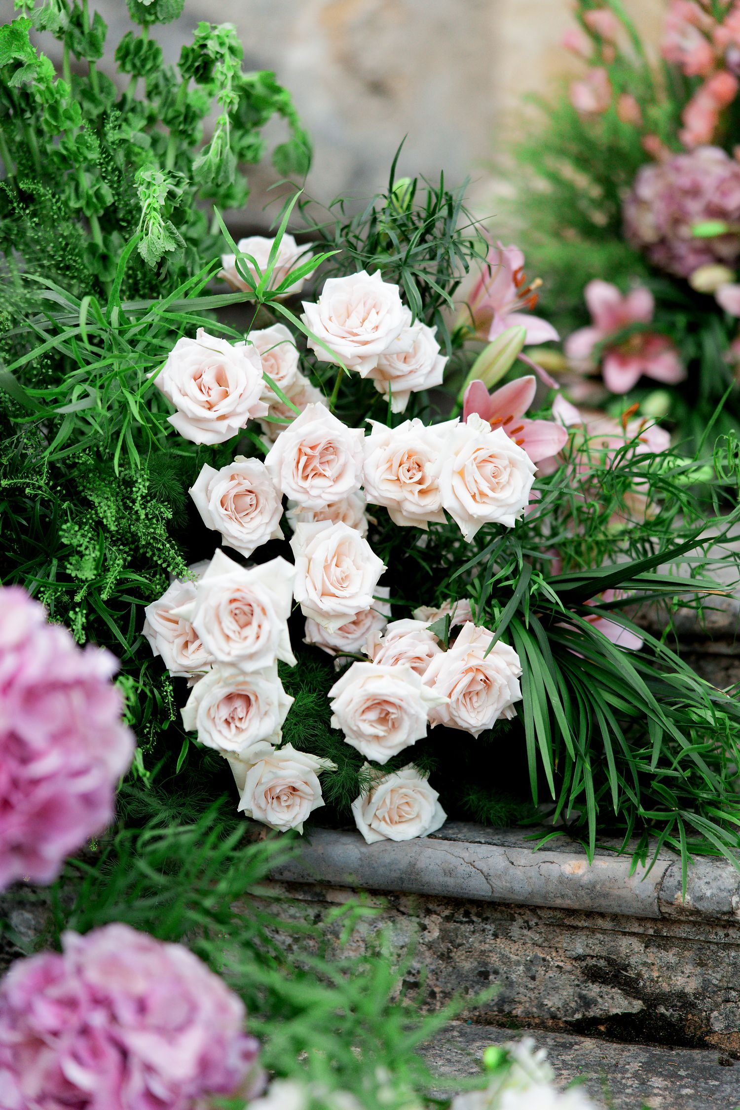 Delicate pale pink roses and green foliage arranged on rustic stone steps in a romantic garden setting.