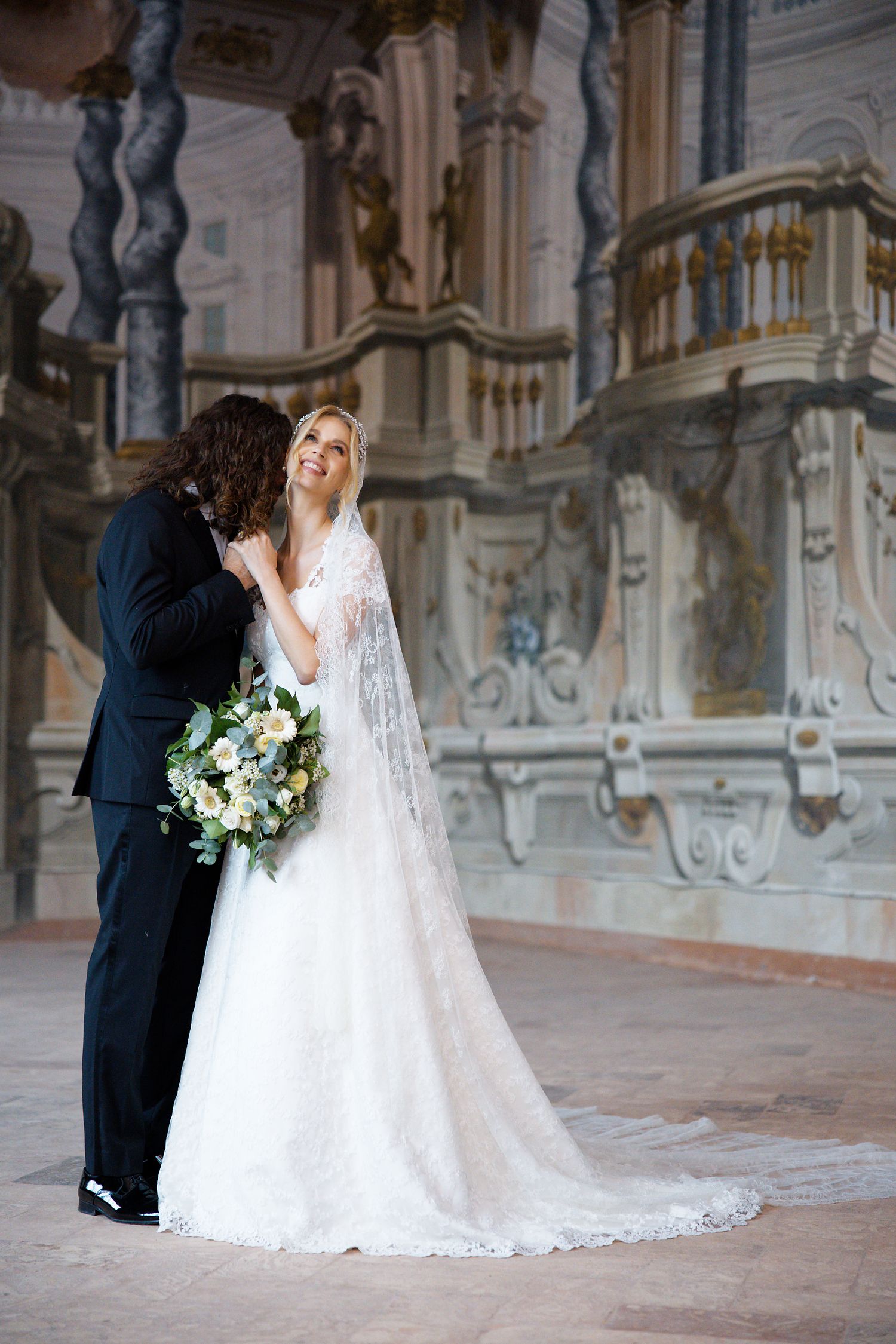A romantic wedding moment captured in an ornate church interior with a beautiful lace wedding gown and bouquet.