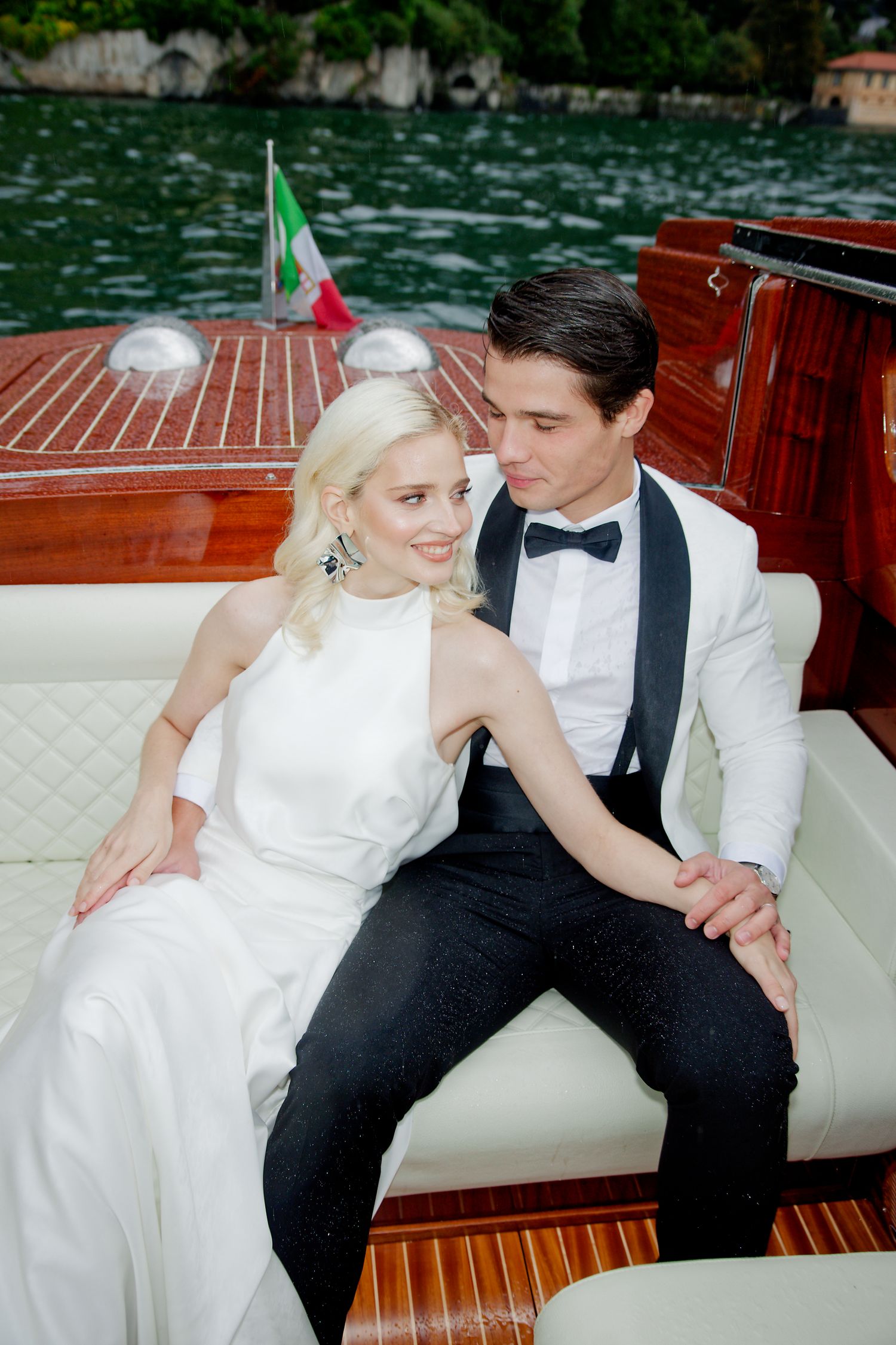 A romantic moment between newlyweds aboard a classic wooden boat with an Italian flag visible.