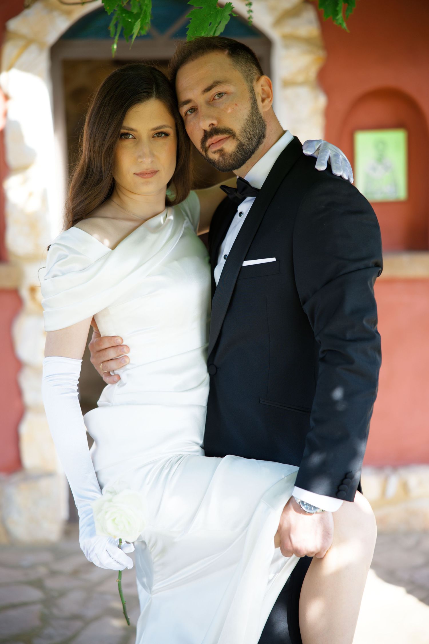 Romantic wedding portraits of couple in white dress and black tuxedo against coral colored wall.