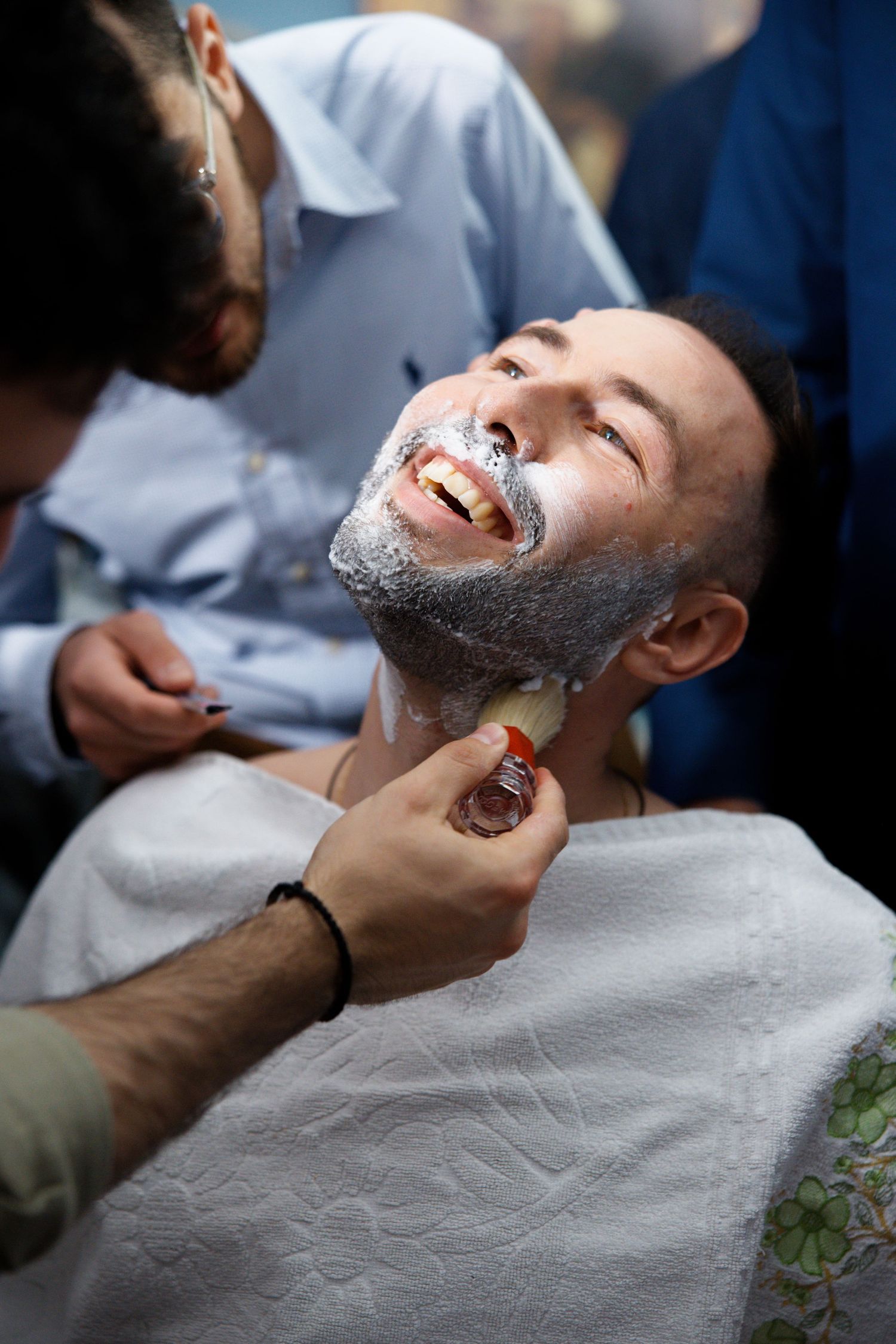 Professional barber carefully shaves a smiling client with traditional straight razor and shaving cream.