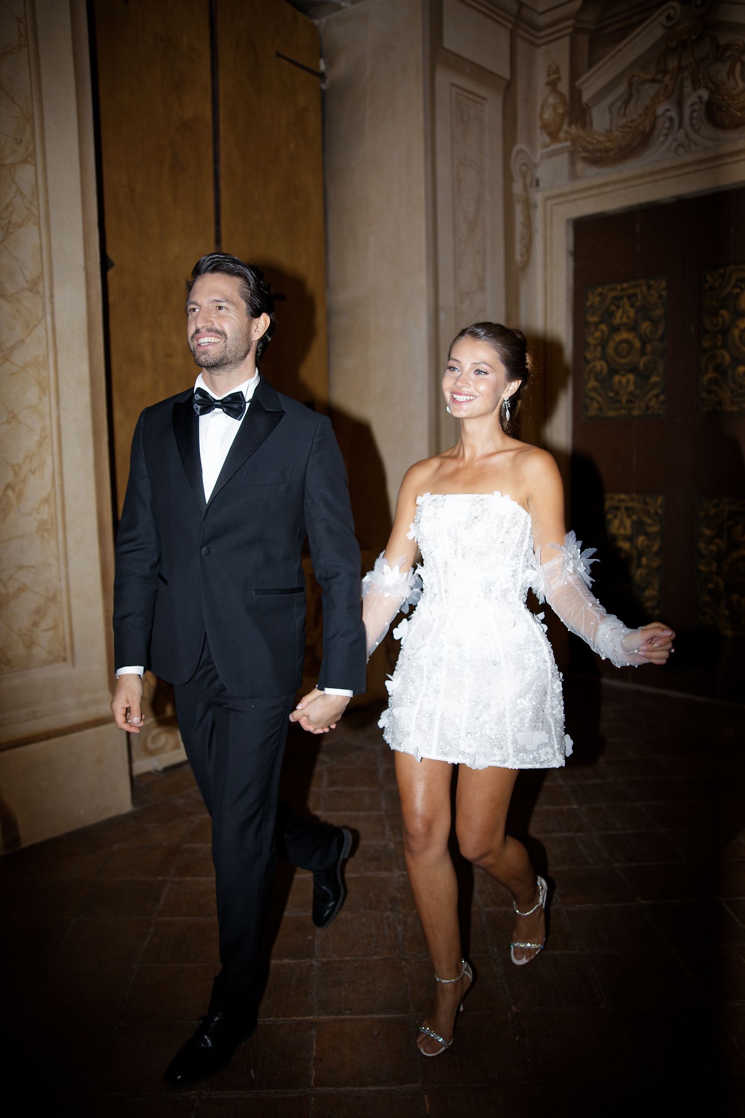 Couple in formal attire walking through elegant hallway at wedding reception.