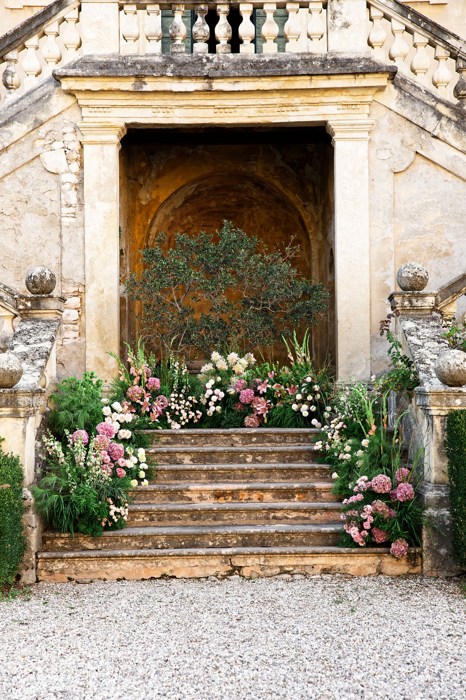 Grand stone staircase adorned with pink and white flowers leading to an ornate archway.