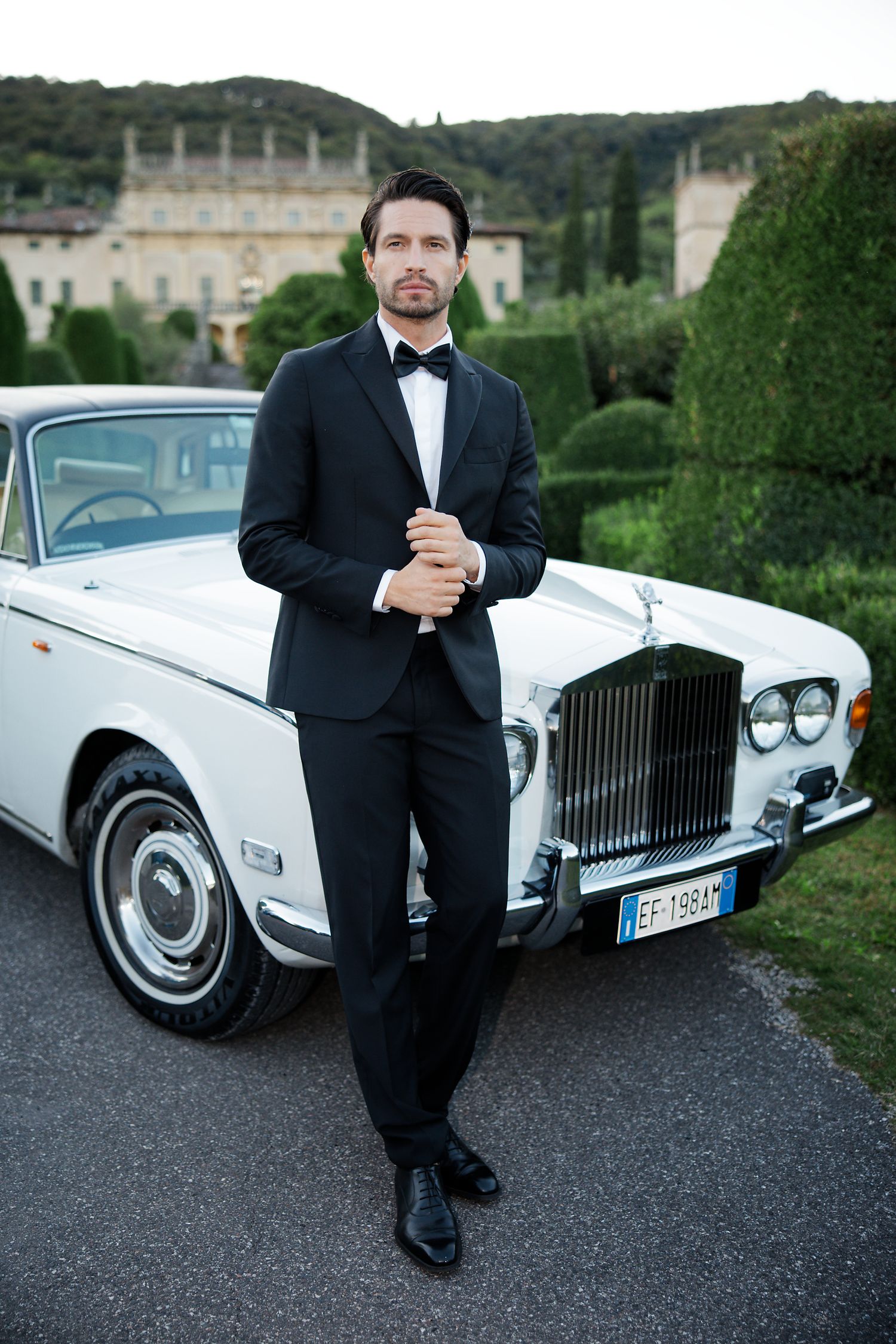 Classic white Rolls-Royce parked in front of an elegant villa with well-manicured gardens.