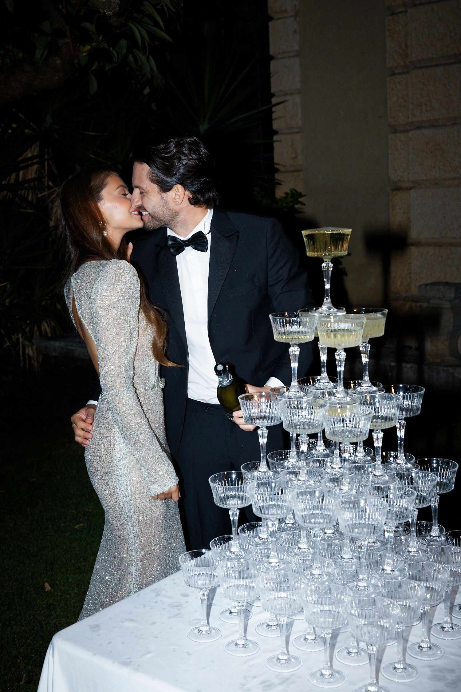Couple sharing intimate moment beside towering champagne glass display.