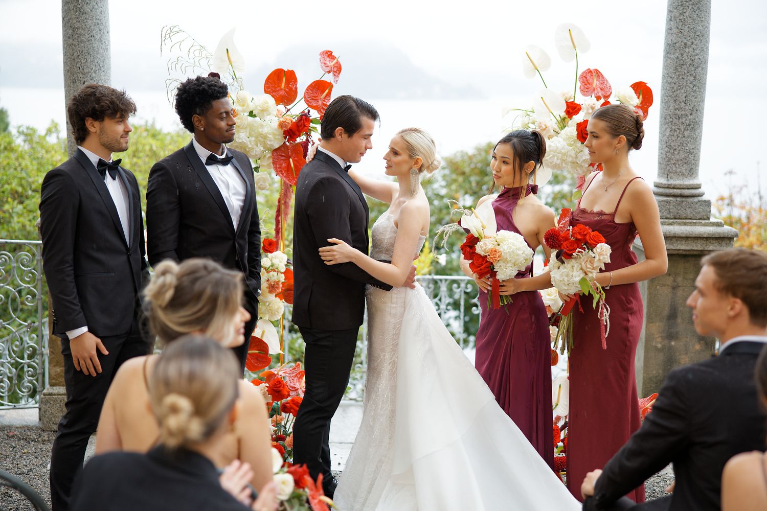 Wedding ceremony under floral arch with coral and white flowers surrounded by wedding party.