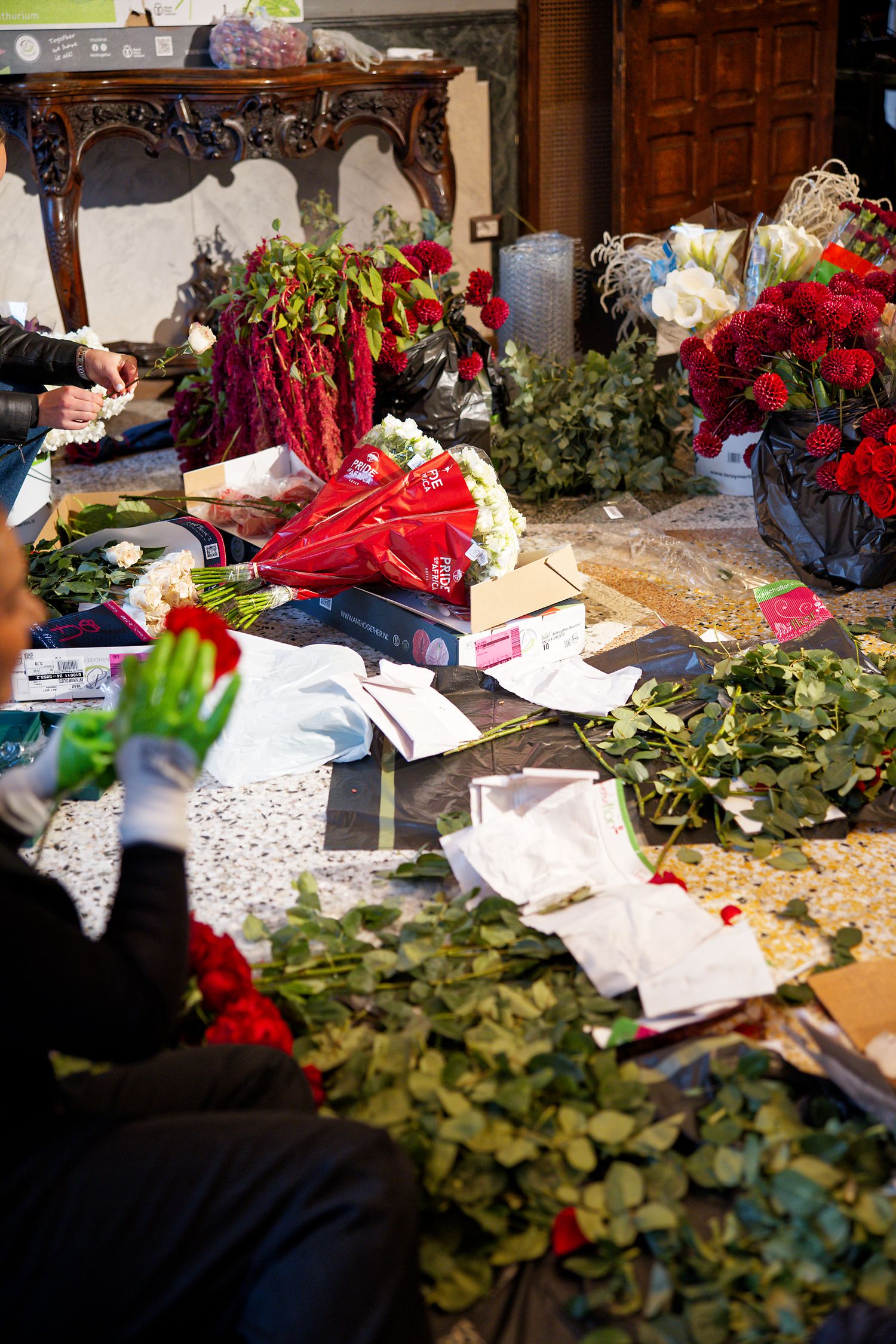 Floral arrangement workspace with red flowers and greenery scattered across ornate wooden table.