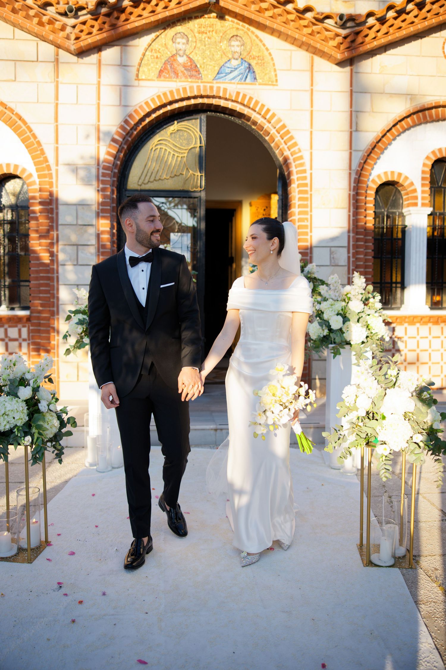 Newlyweds walking together through arched hallway decorated with floral arrangements.