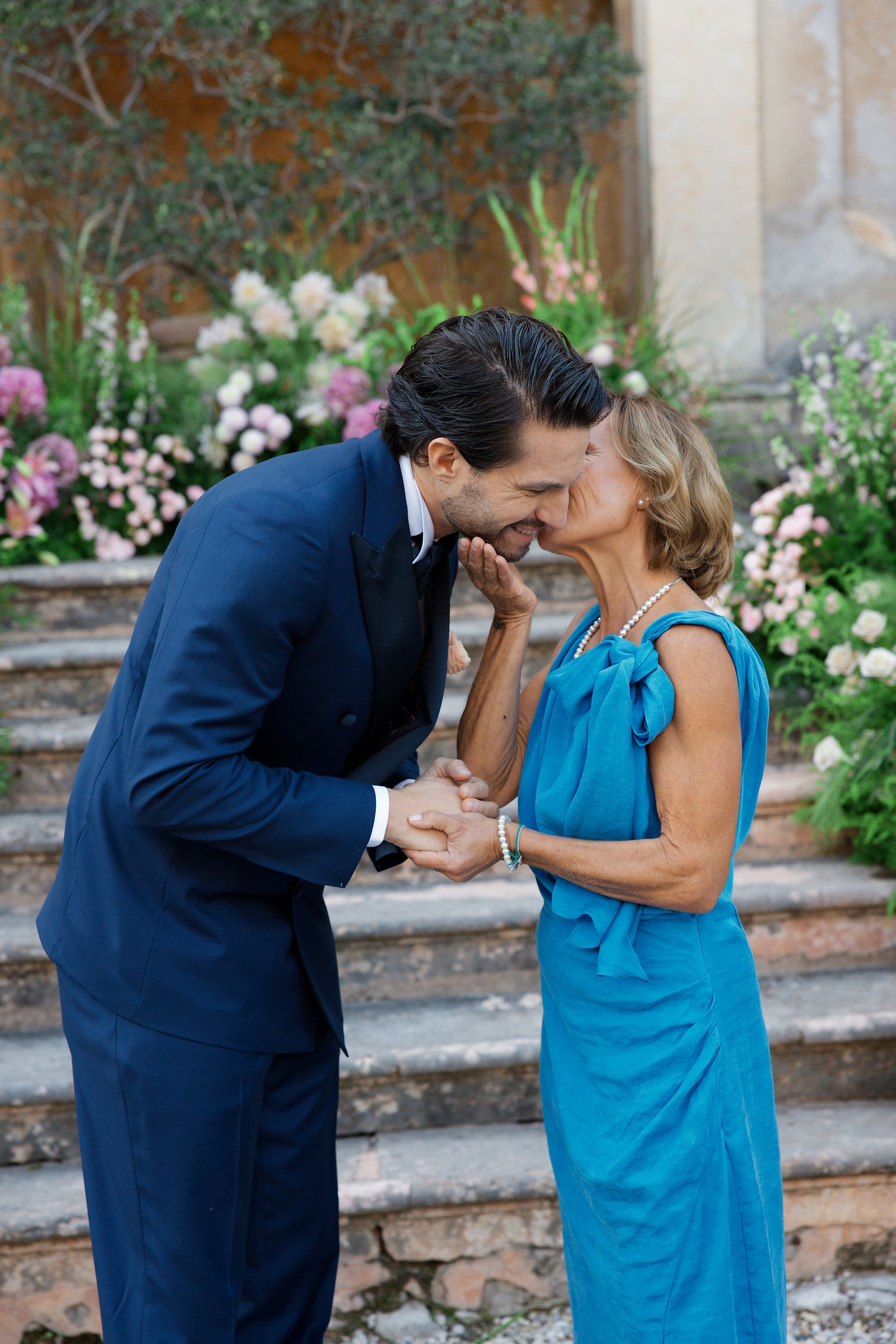 A joyful moment shared between a person in a navy suit and another in a bright blue dress in a garden setting.