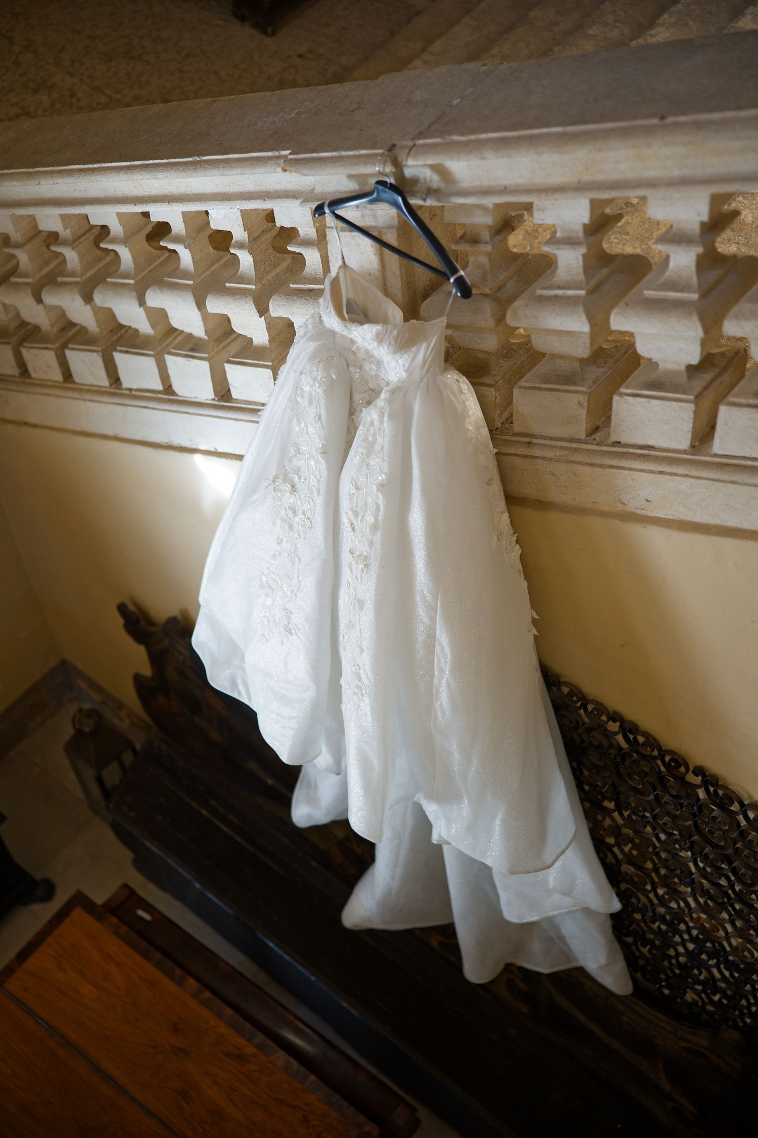 An elegant white wedding dress hangs on display against an ornate architectural wall detail.
