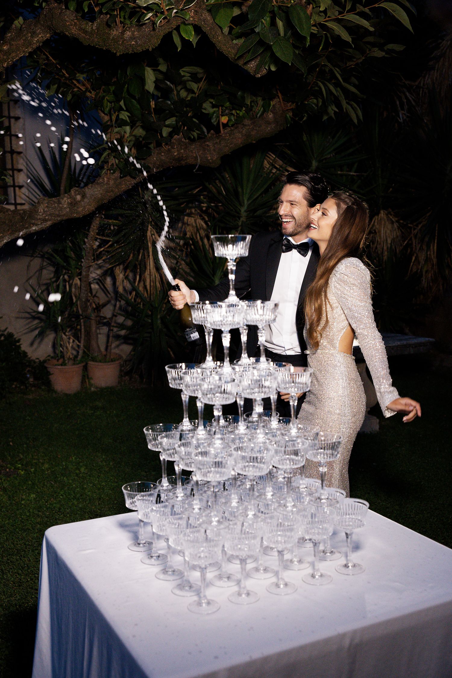 Wedding celebration with champagne tower being poured at an outdoor evening reception.