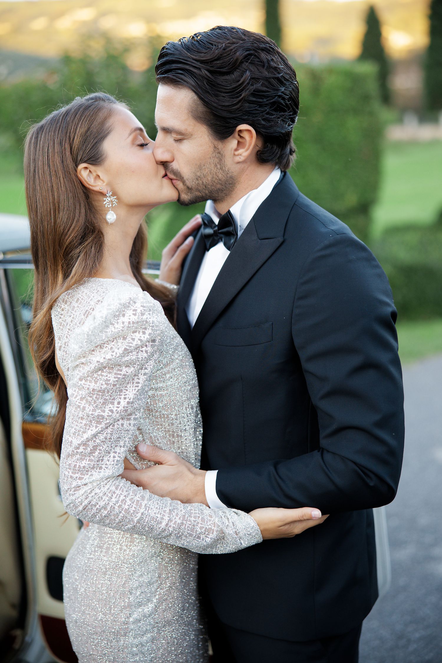 A romantic moment between a couple in formal attire sharing an intimate embrace outdoors at dusk.