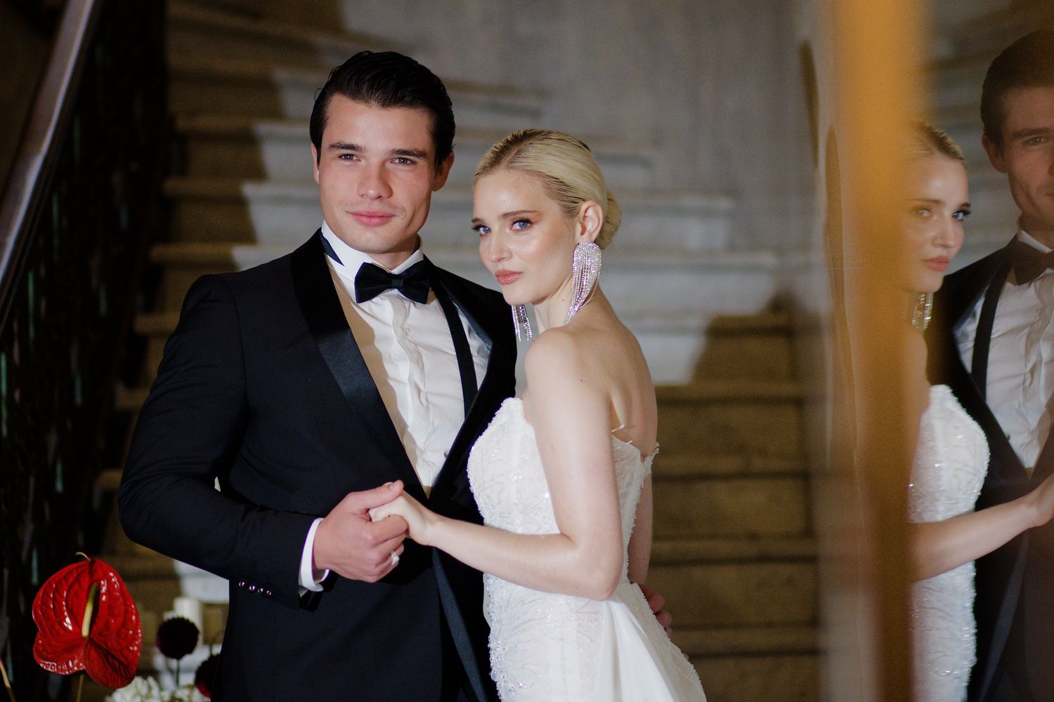 An elegant formal couple poses on a grand staircase during a wedding celebration.