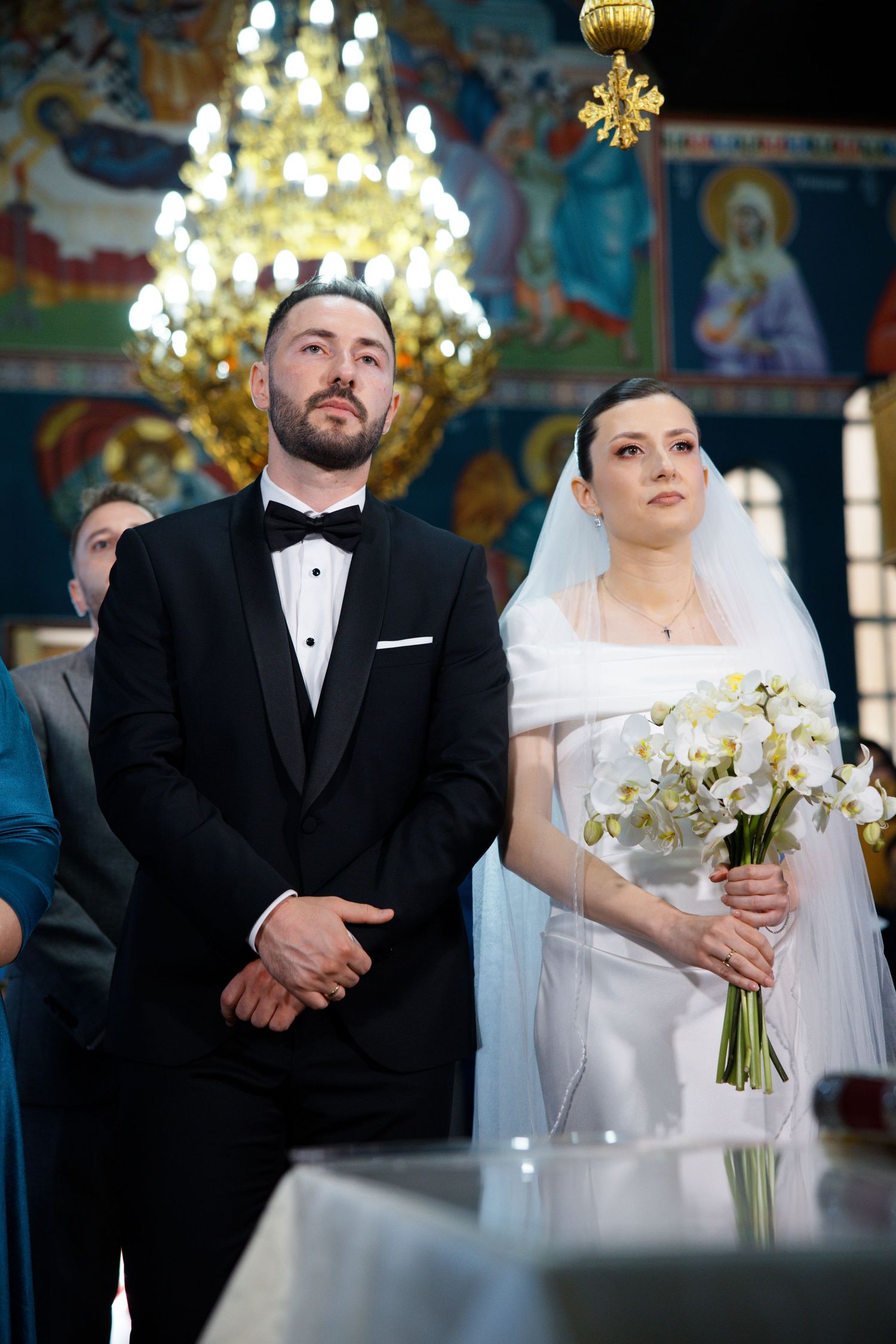 Wedding ceremony in an ornate church with chandeliers and religious artwork.