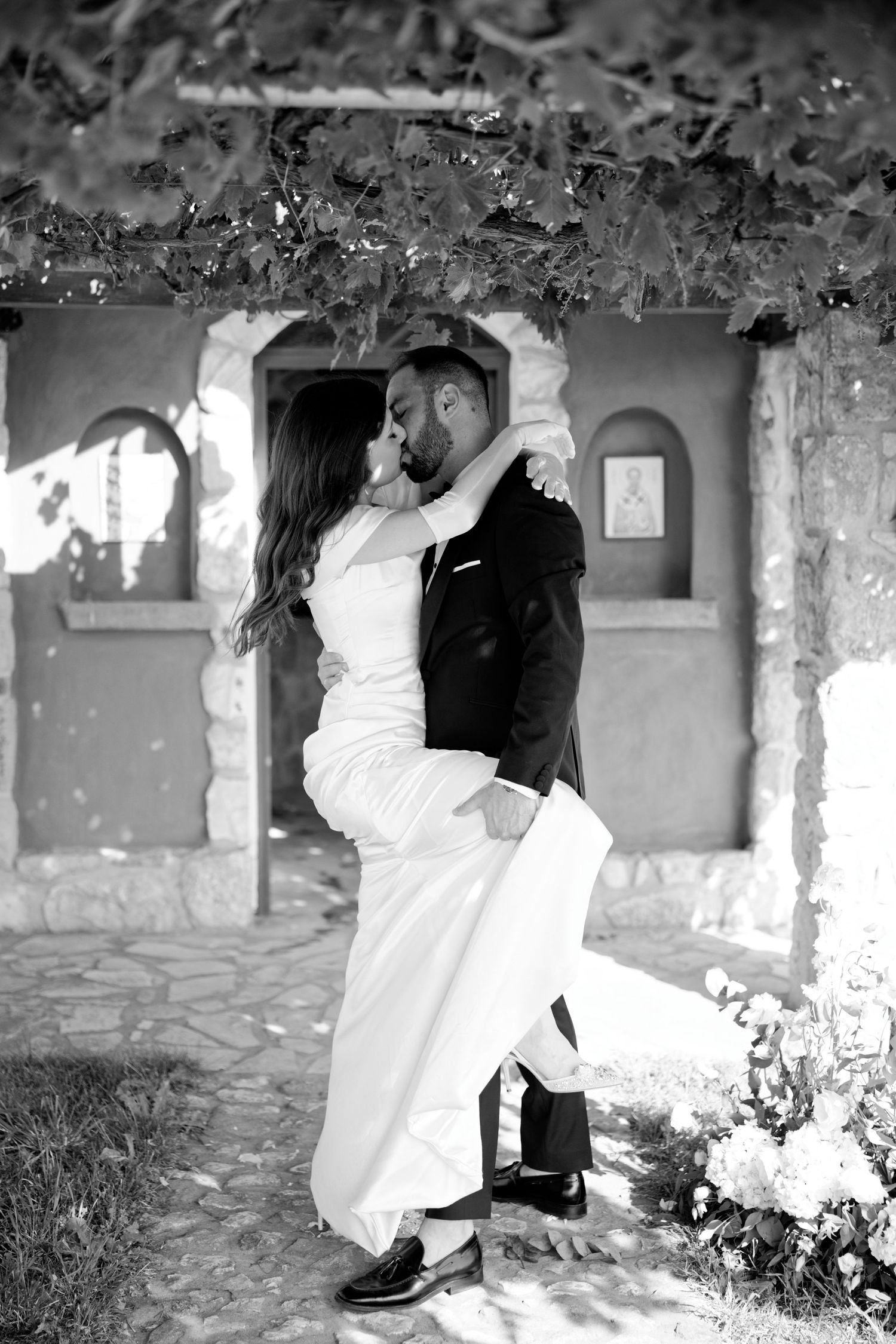 Black and white romantic wedding portrait with couple embracing against stone wall.