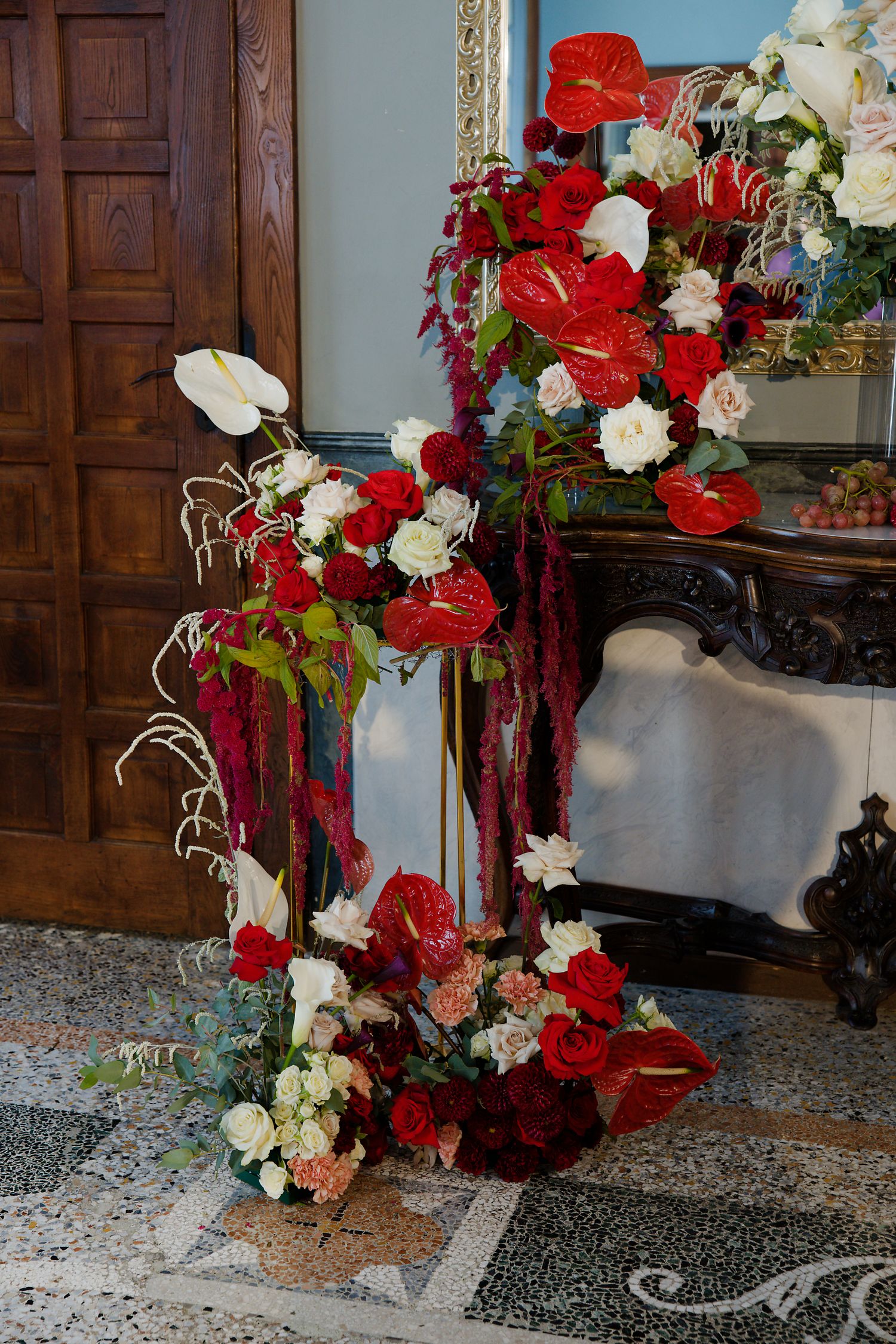 Dramatic red and white floral arrangement with anthurium flowers and roses cascades down against wooden paneling.