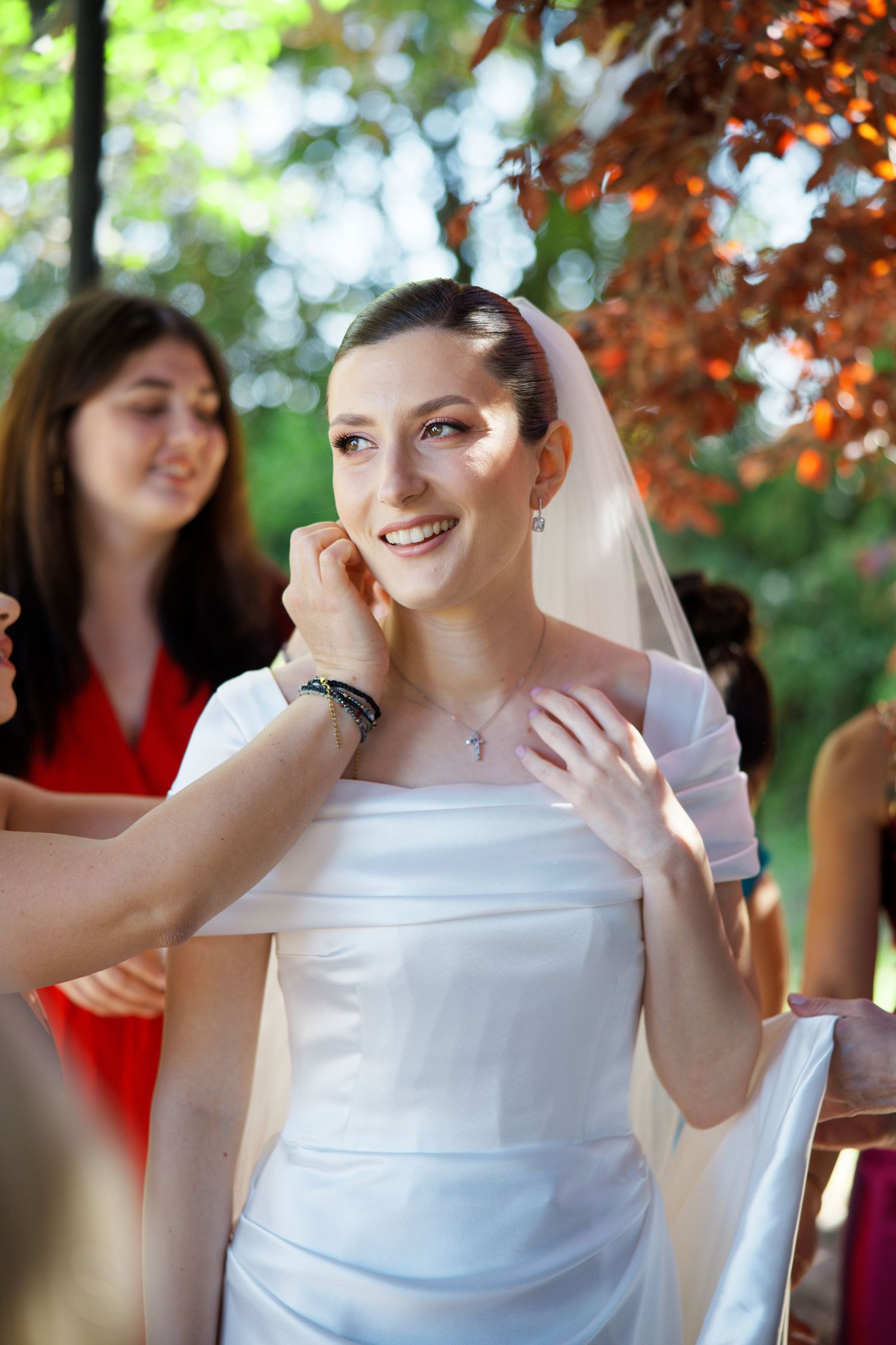 A radiant bride in a classic white gown shares a joyful moment during wedding preparations outdoors.
