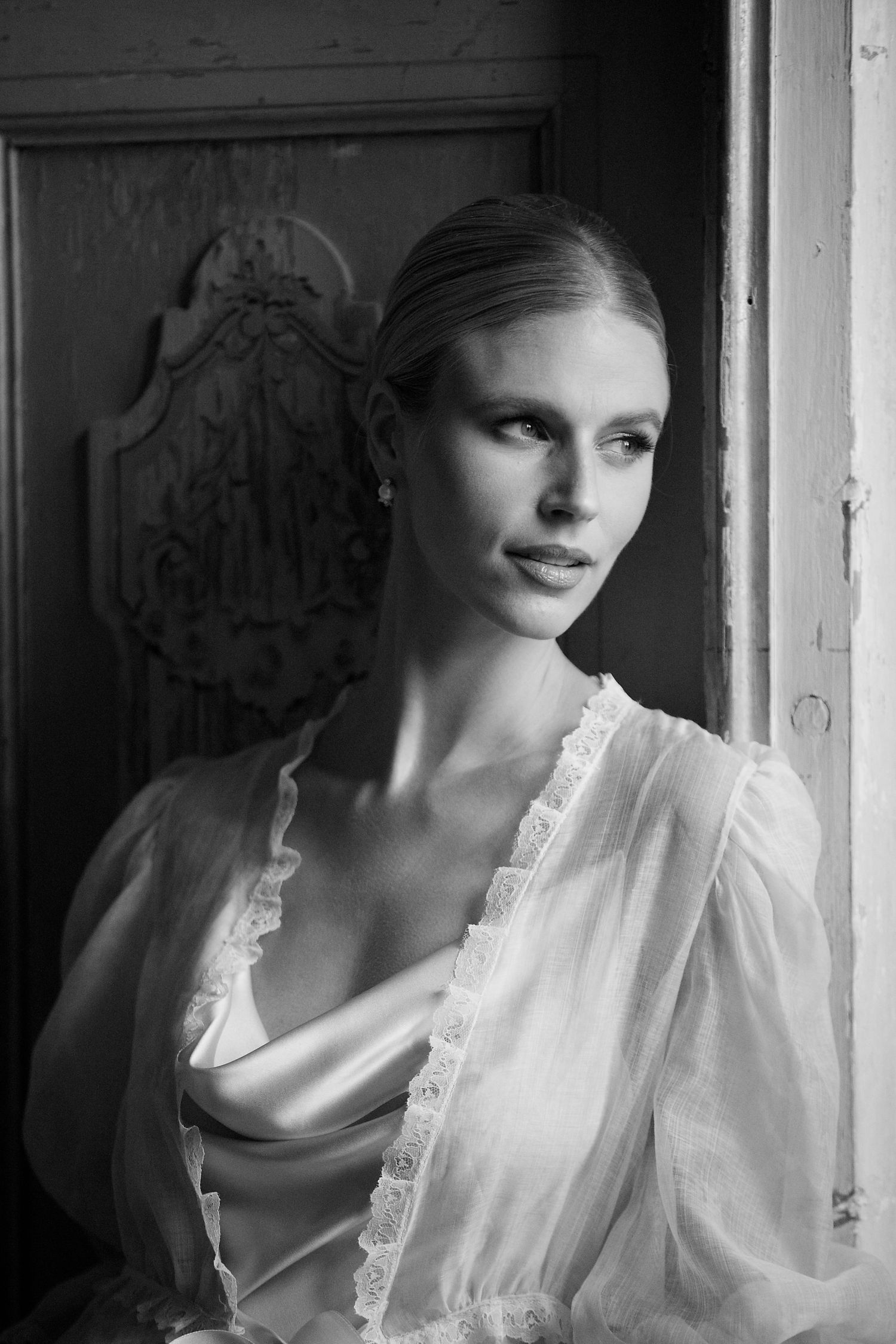 Elegant bridal portrait in black and white showing delicate lace robe by vintage doorway.
