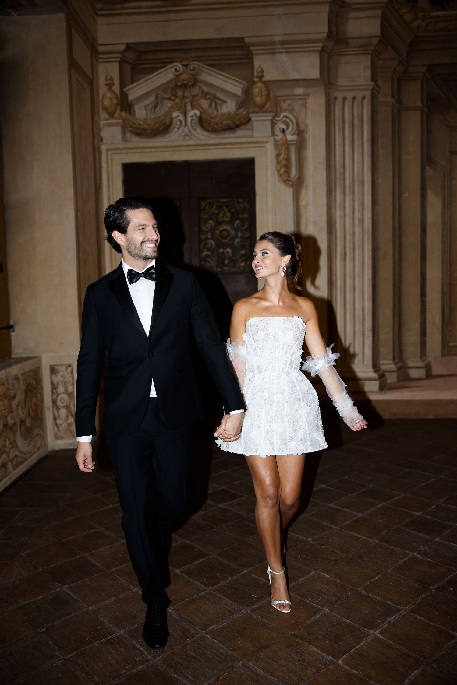 Newlyweds walking through ornate hallway during wedding celebration.