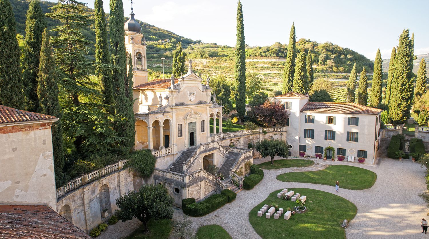 An elegant villa estate with cypress trees and manicured gardens sits nestled in the Italian countryside.