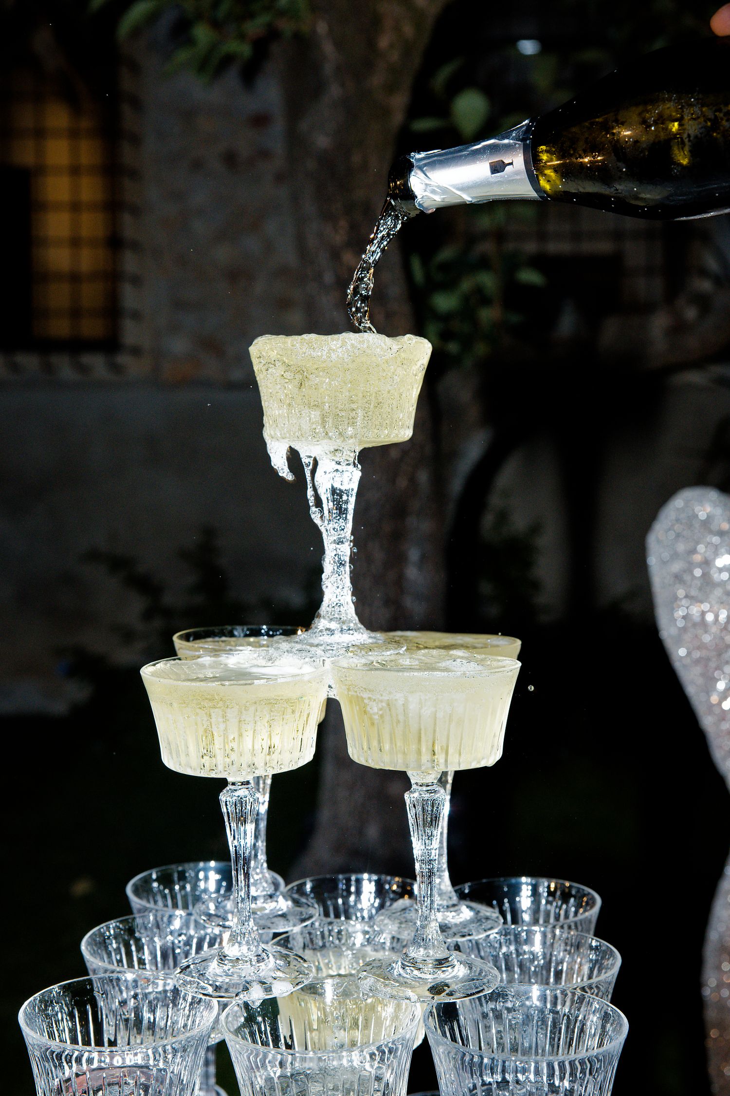 Champagne being poured into a tower of elegant crystal coupe glasses arranged in tiers for a celebration.